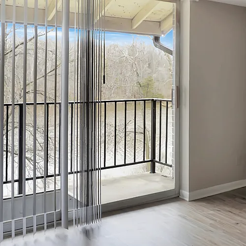 Bright and open living area with hardwood floors and floor-to-ceiling windows leading to a scenic balcony view.
