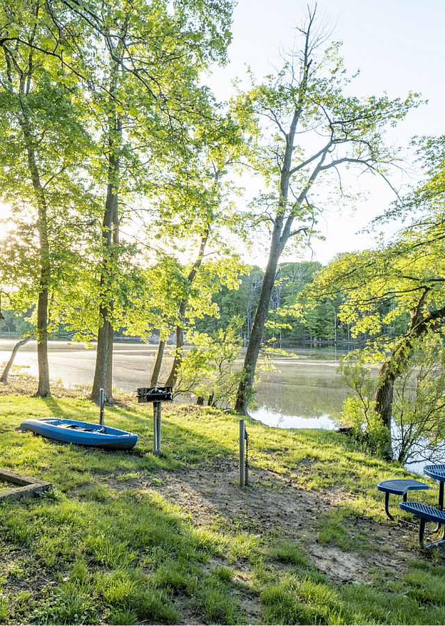 Tranquil lakeside area with lush greenery, a picnic table, and a canoe by the water's edge.