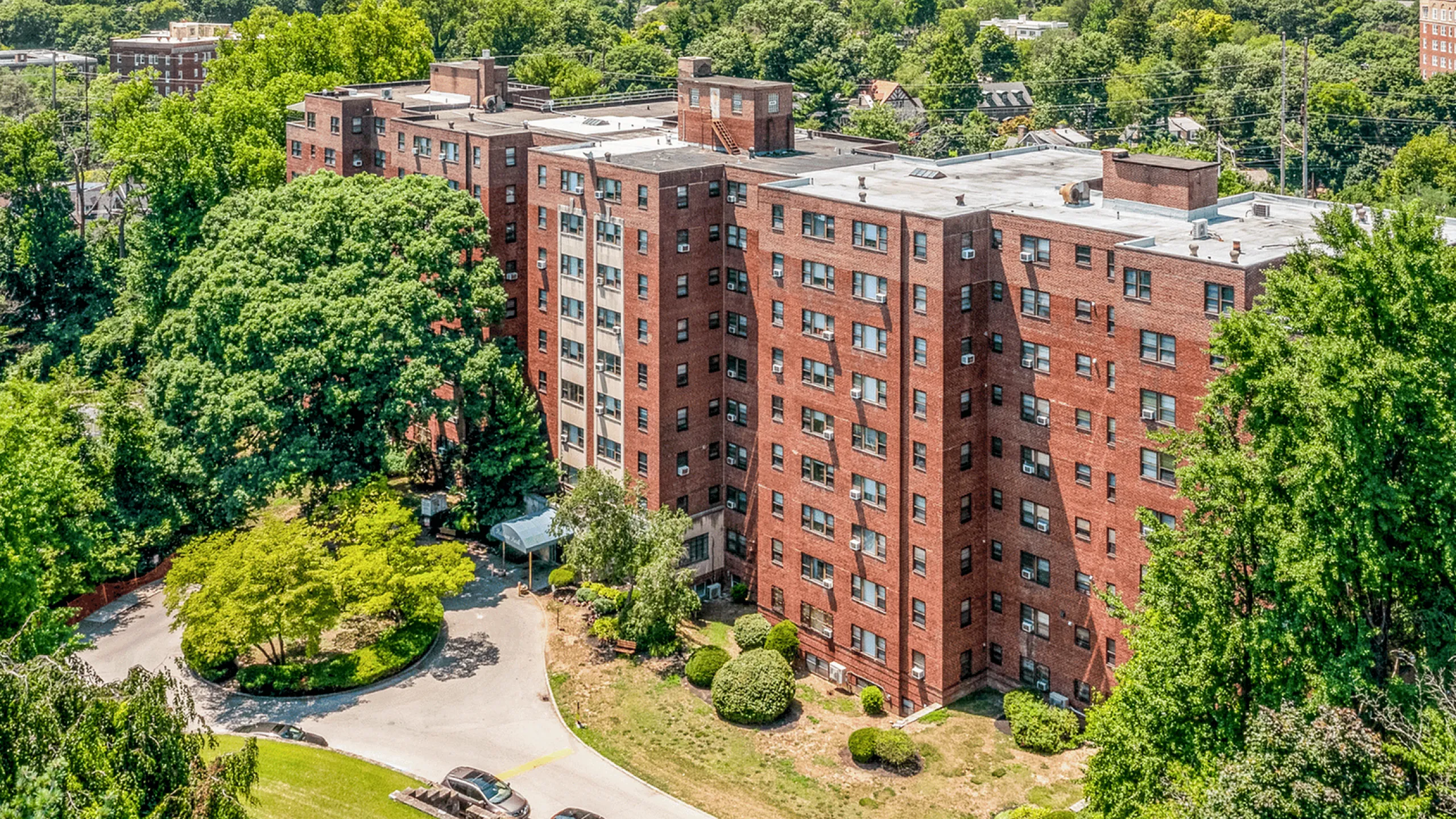 A spacious red brick apartment building surrounded by lush trees and landscaped greenery.