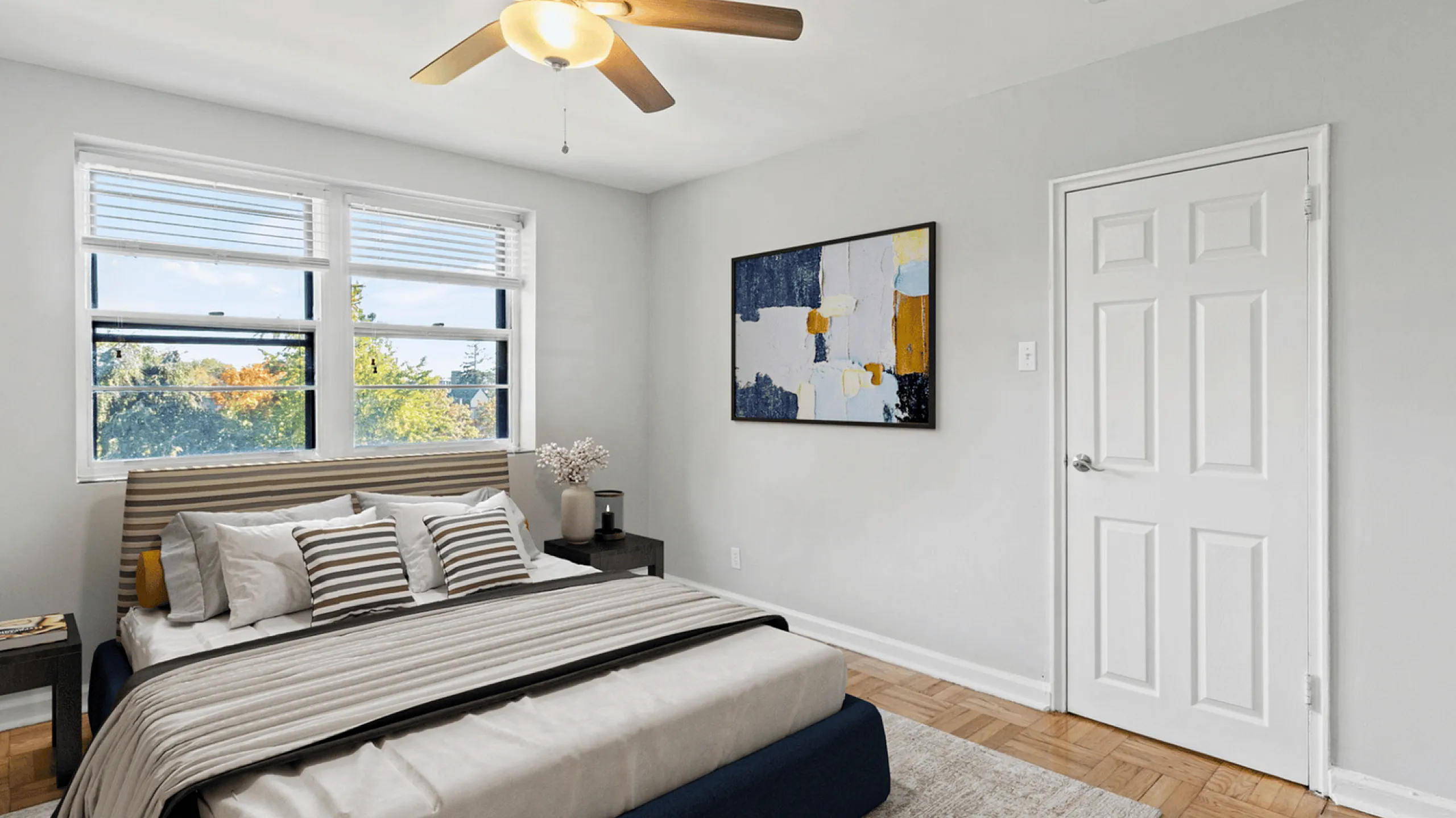 Sunny bedroom with a stylish ceiling fan, modern art, and large windows offering a scenic view.