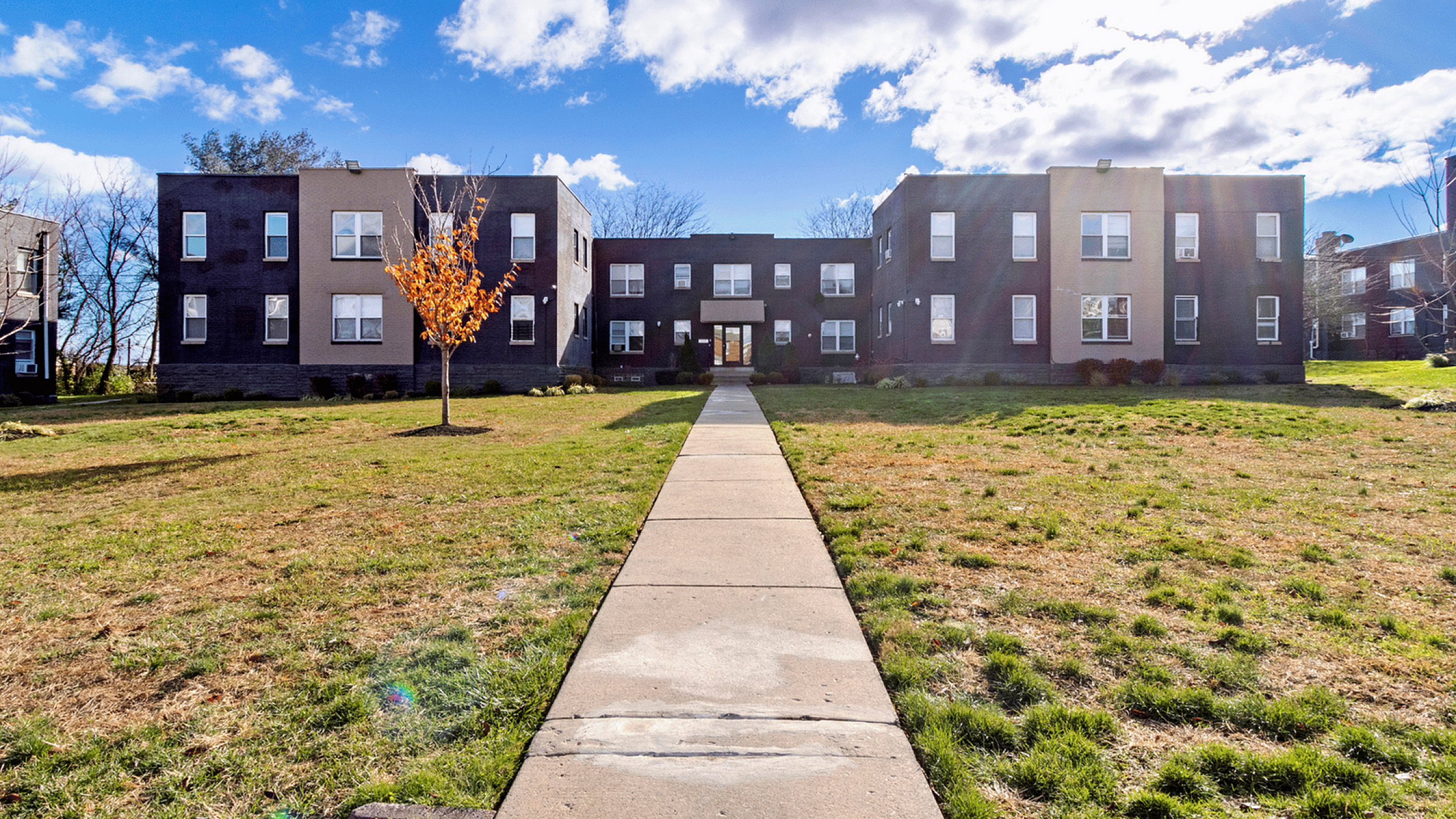Sunny view of a charming apartment building with a spacious lawn and a central walkway.