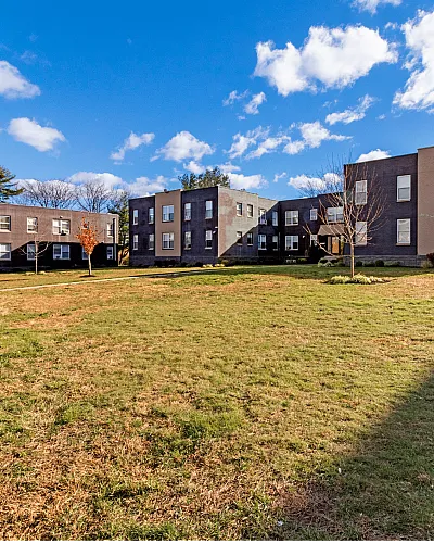 Exterior view of a modern apartment complex with a large green lawn and clear blue sky.