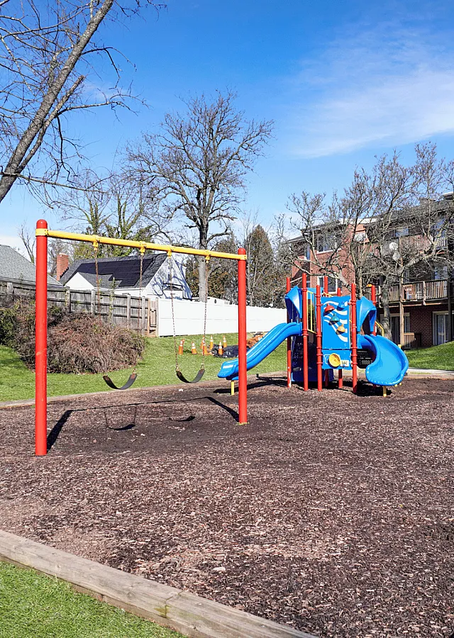 Inviting playground with swings and a vibrant slide surrounded by apartment buildings and greenery.