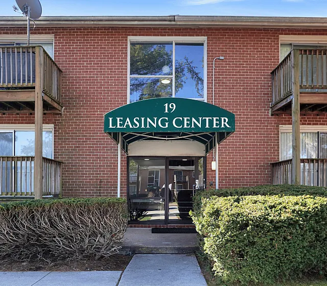 Inviting entrance of a brick building featuring a leasing center with green awning and well-maintained landscaping.