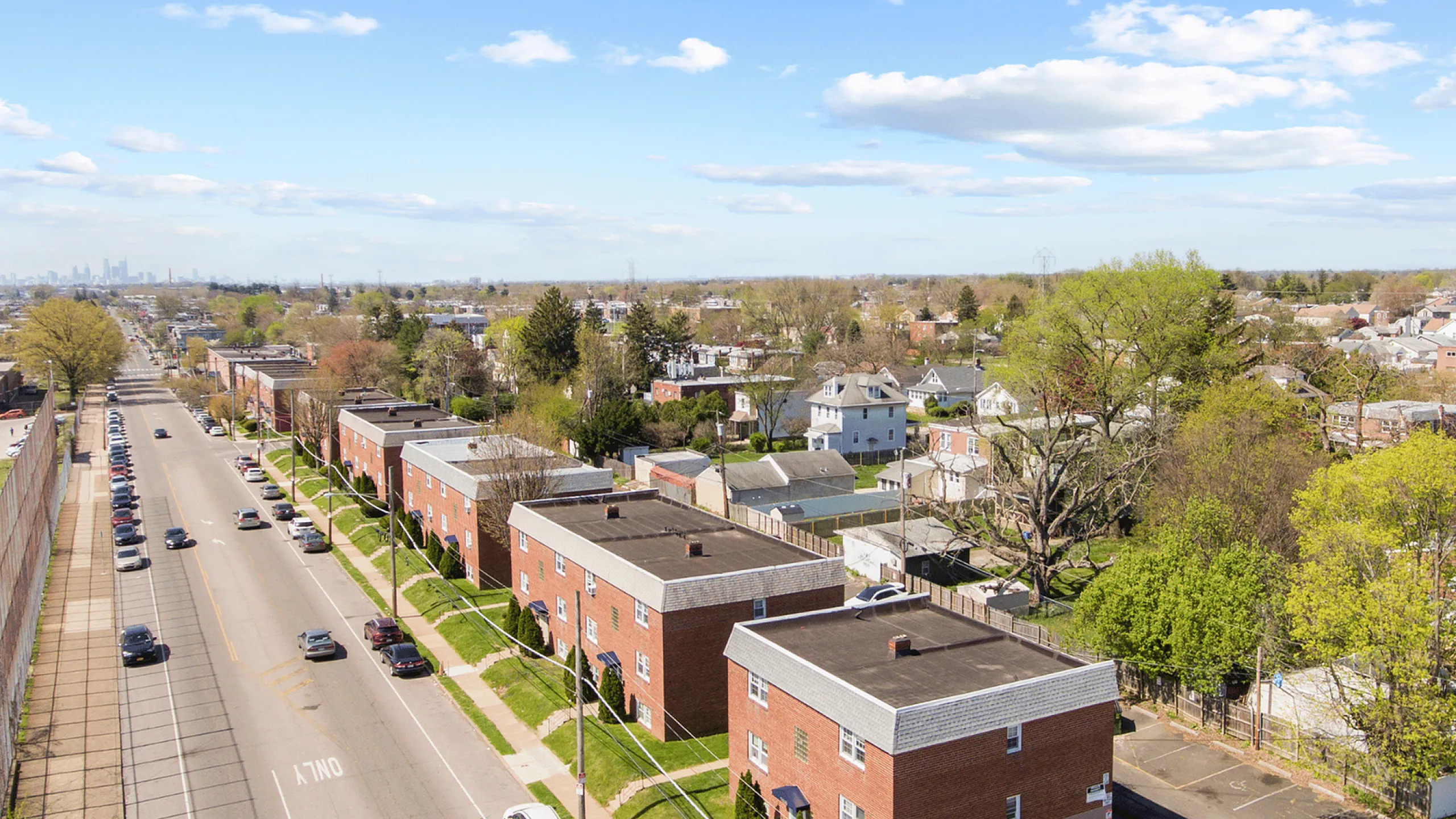 Aerial view of a charming suburban neighborhood with brick apartment buildings and tree-lined streets under a bright blue sky.