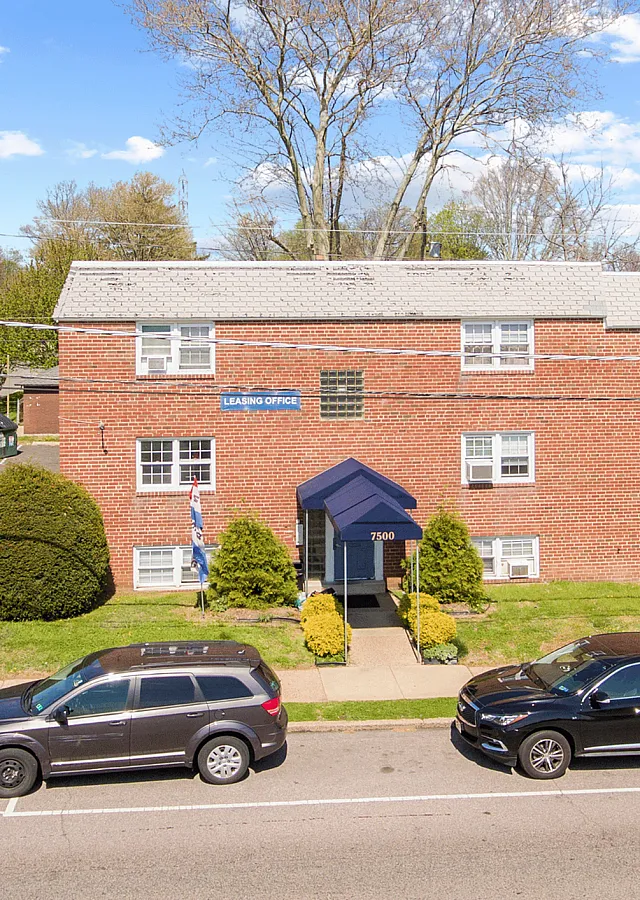 A welcoming brick apartment building with a blue awning and well-maintained landscaping.