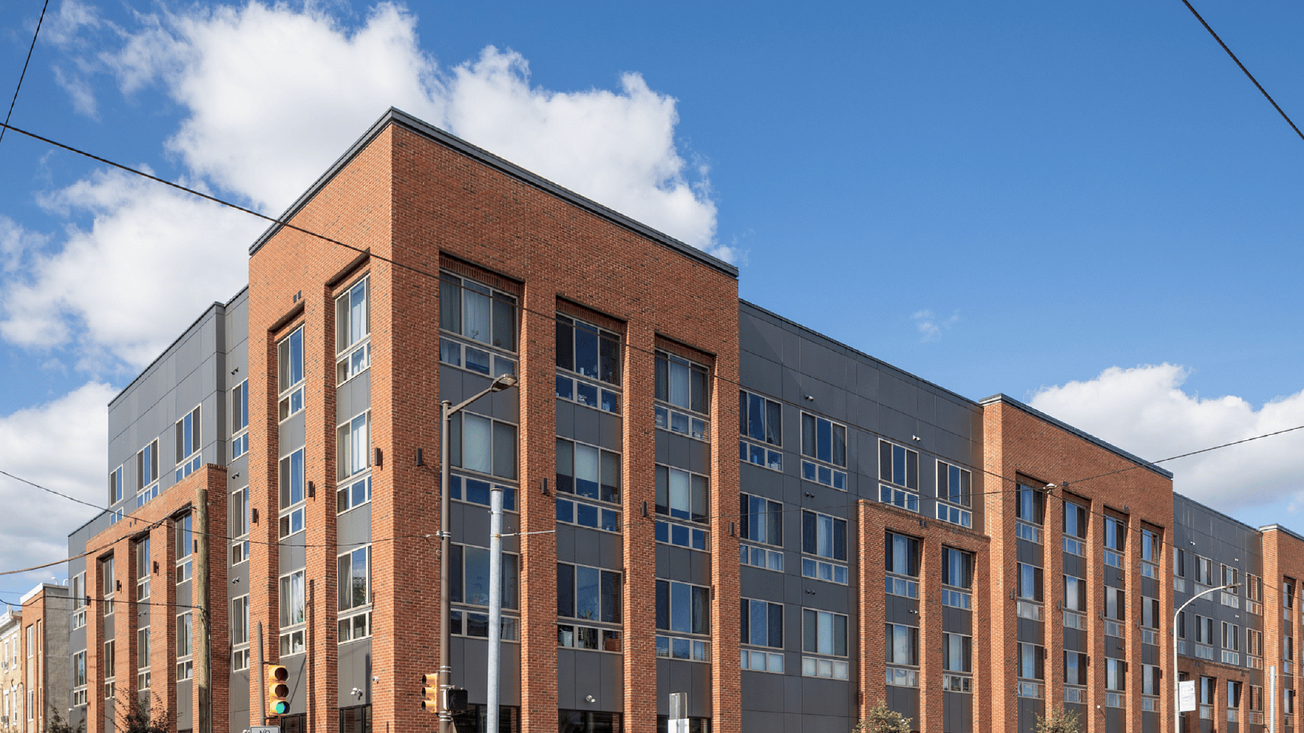 Modern brick and glass apartment building under a clear blue sky, featuring a dynamic corner architecture.