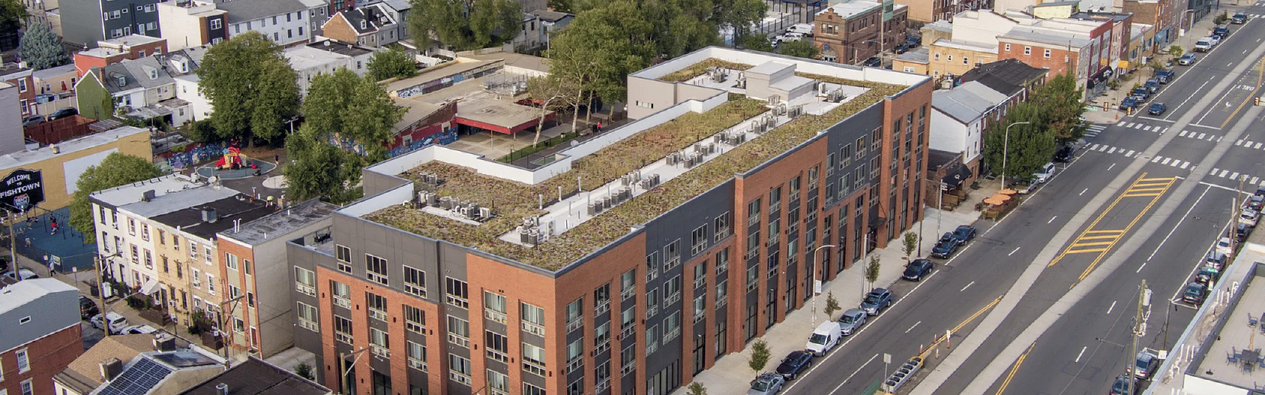Aerial view of a modern apartment complex with a lush rooftop garden nestled in a bustling city neighborhood.