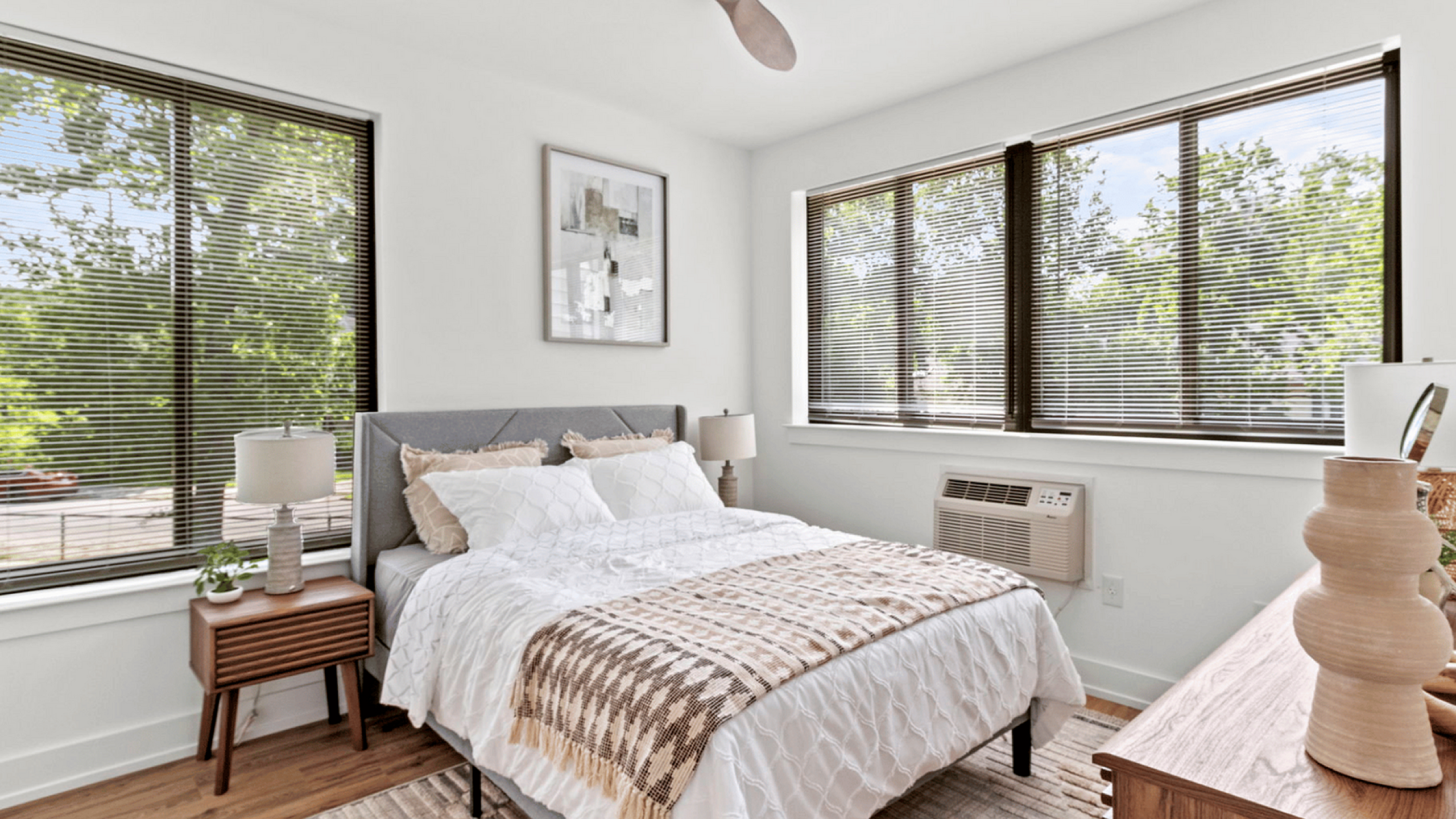 Bright and cozy bedroom with a stylish double bed, modern decor, and large windows revealing lush greenery.