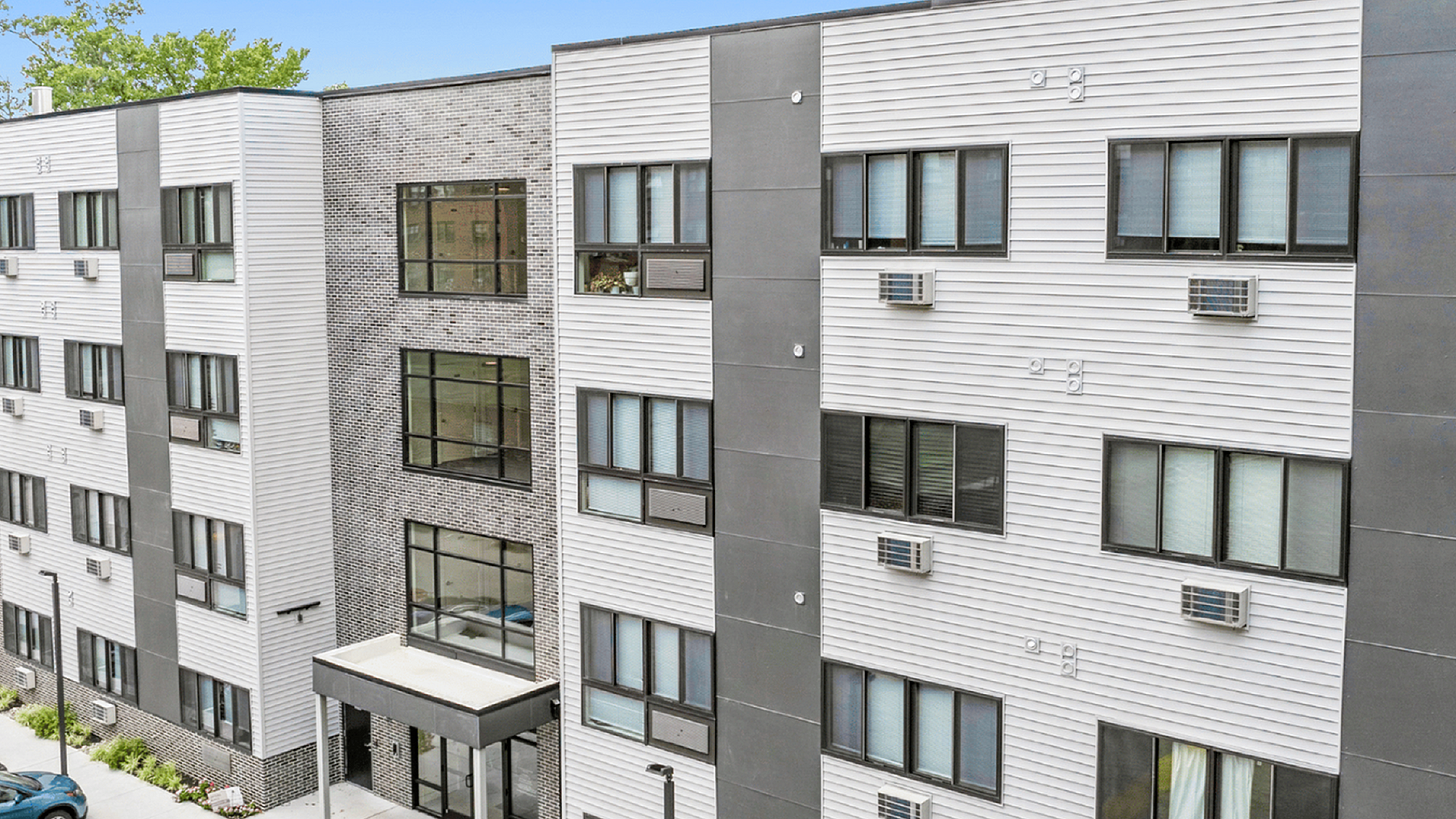 Modern apartment building with multiple floors, large windows, and a well-maintained parking area.