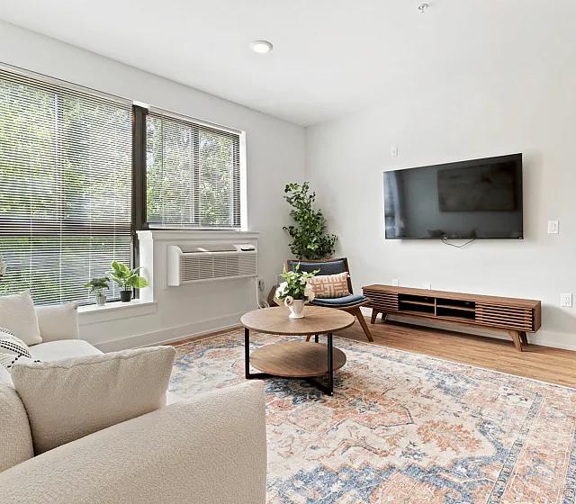 Bright and stylish living room with cozy beige sofa, wooden coffee table, large TV, and lush greenery.