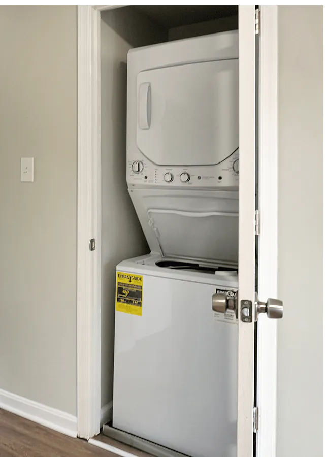 Functional laundry area with a stacked washer and dryer in a modern apartment hallway.