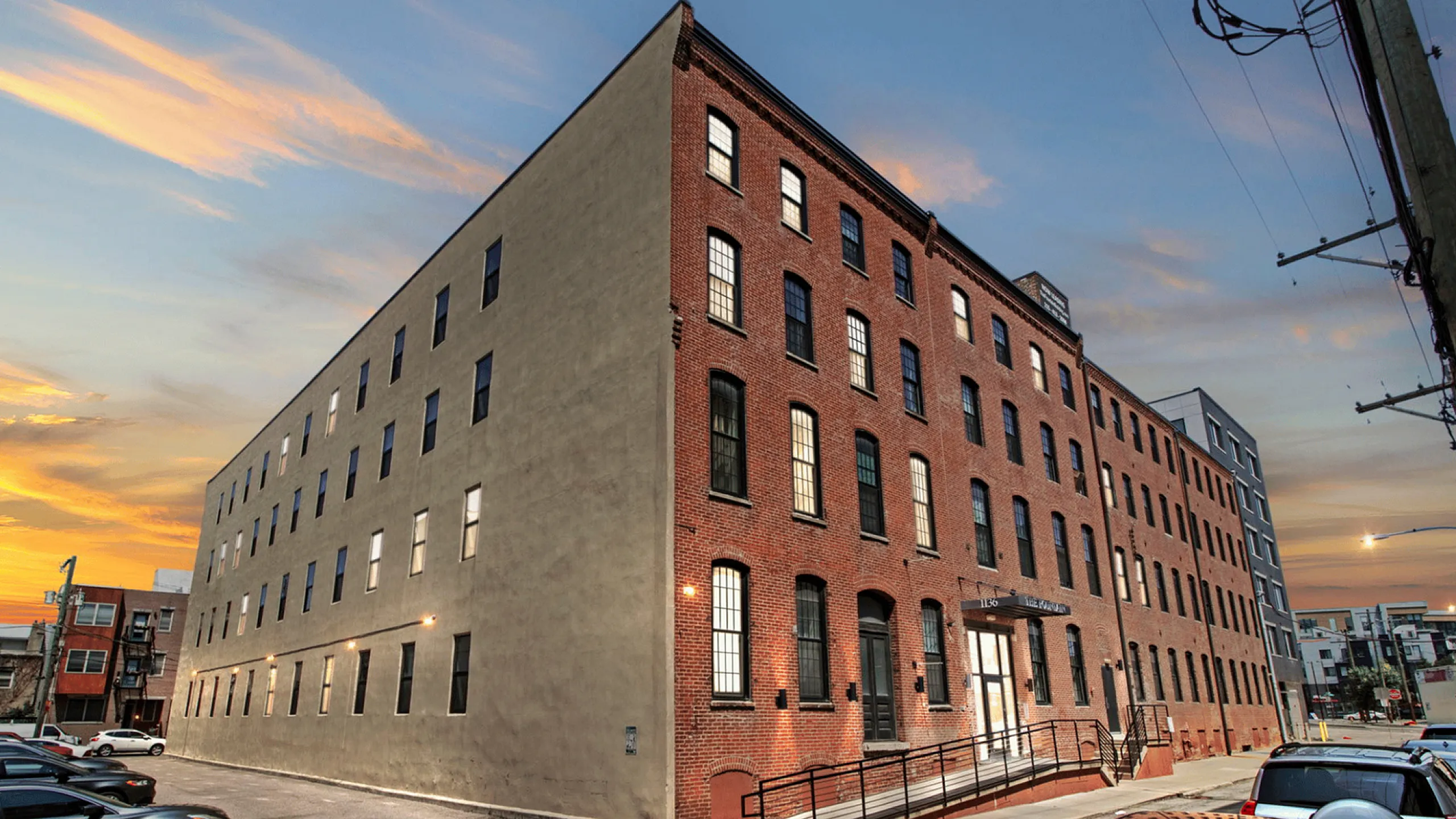 Charming brick apartment building with large windows and urban street view at sunset.