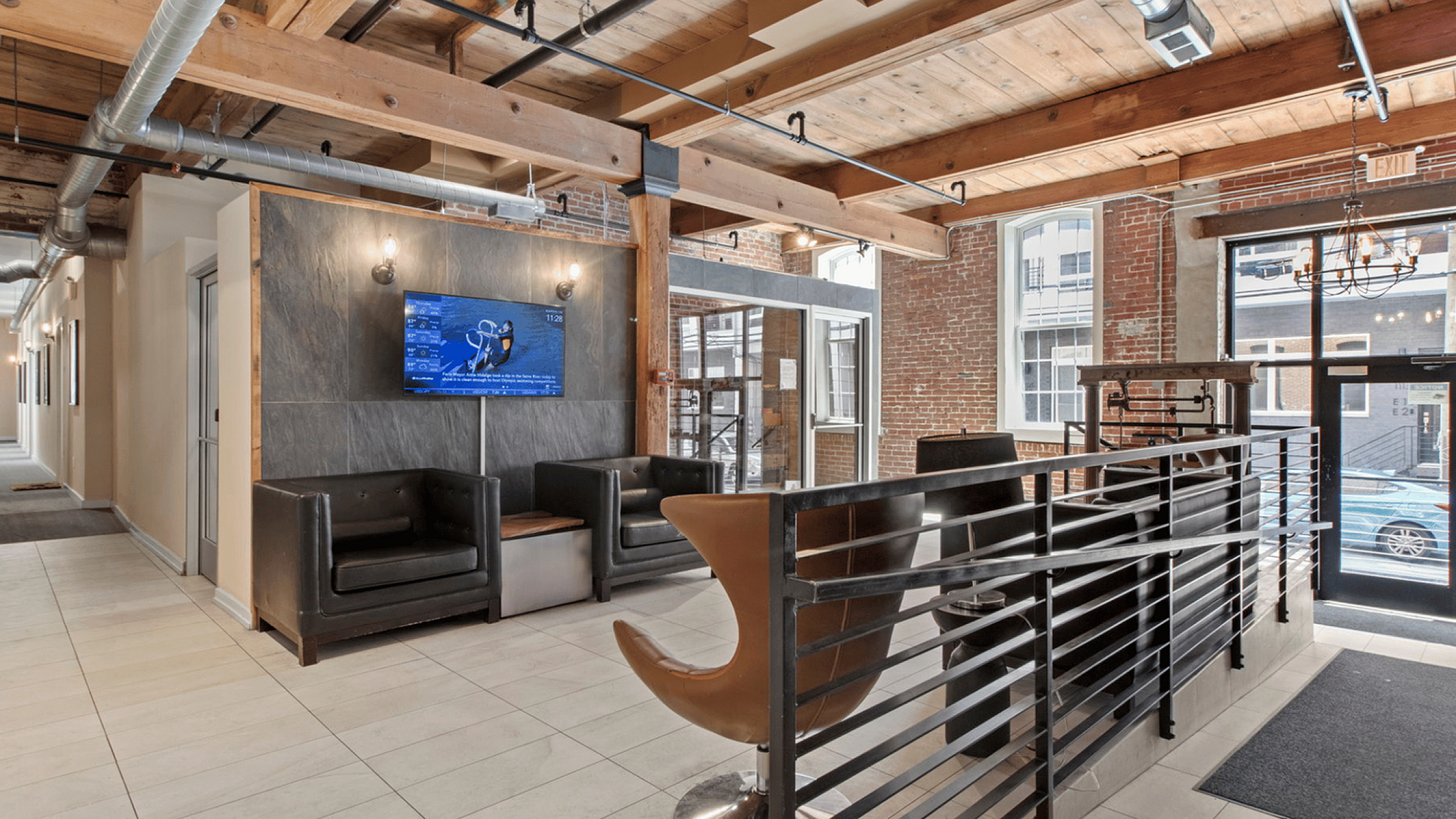 Stylish lobby with industrial design featuring exposed beams, modern seating, and a wall-mounted TV.
