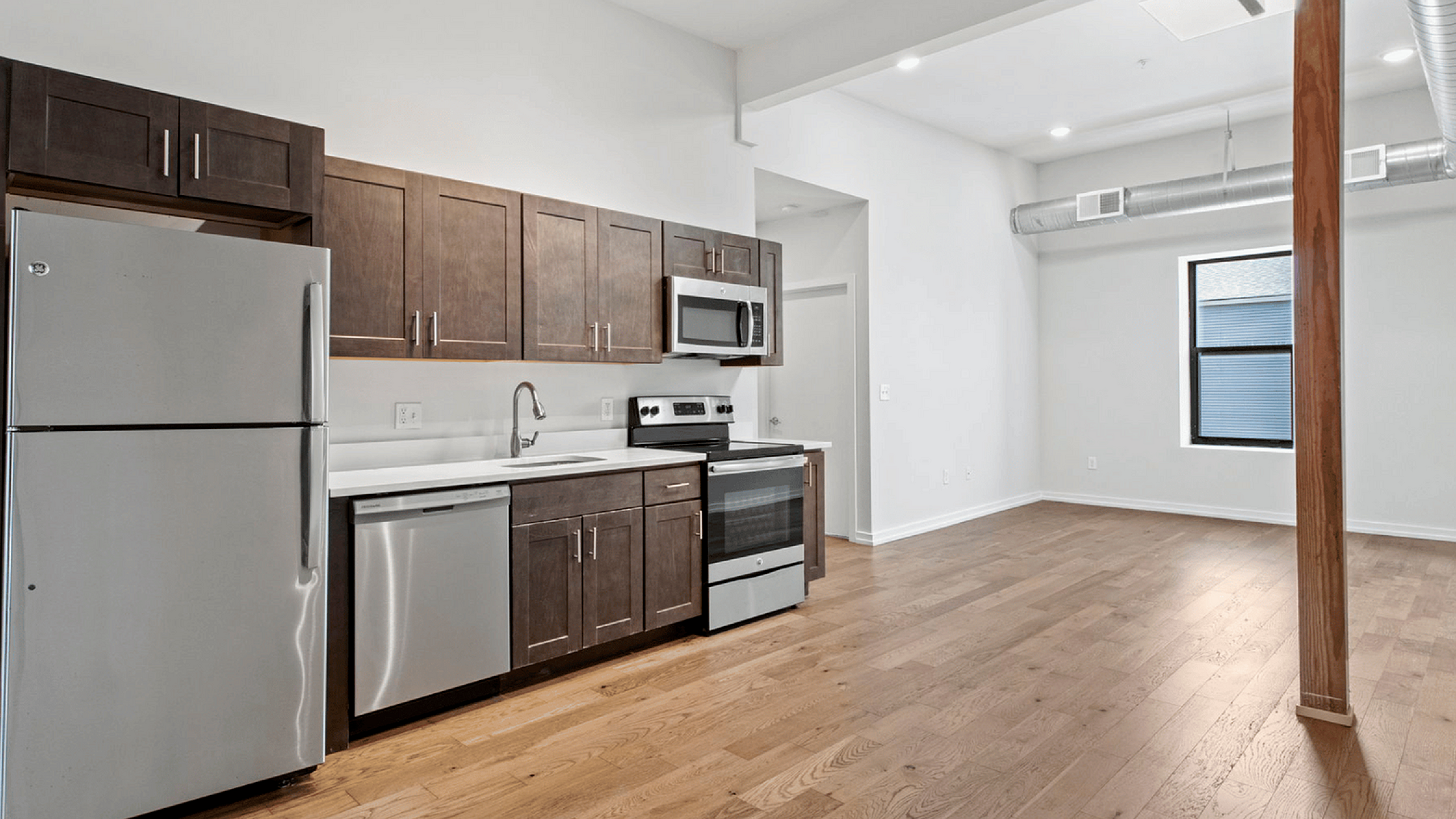 Modern kitchen with stainless steel appliances, dark wood cabinetry, and open living area.