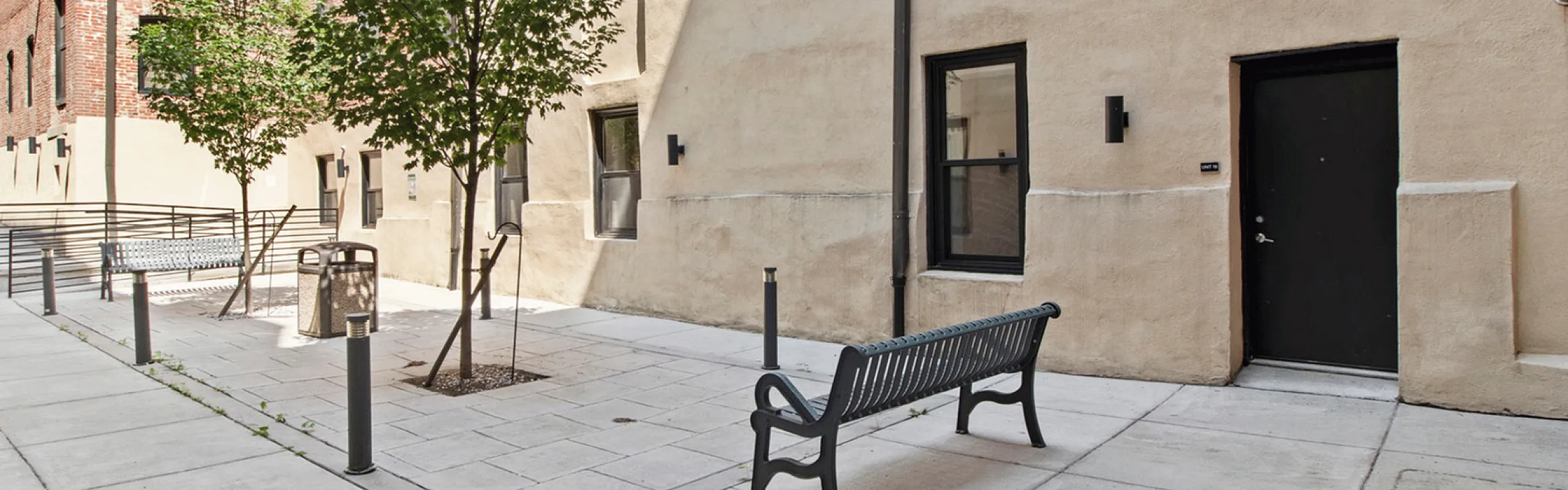 Inviting apartment exterior with a stylish bench, lush trees, and warm brick and stucco walls.