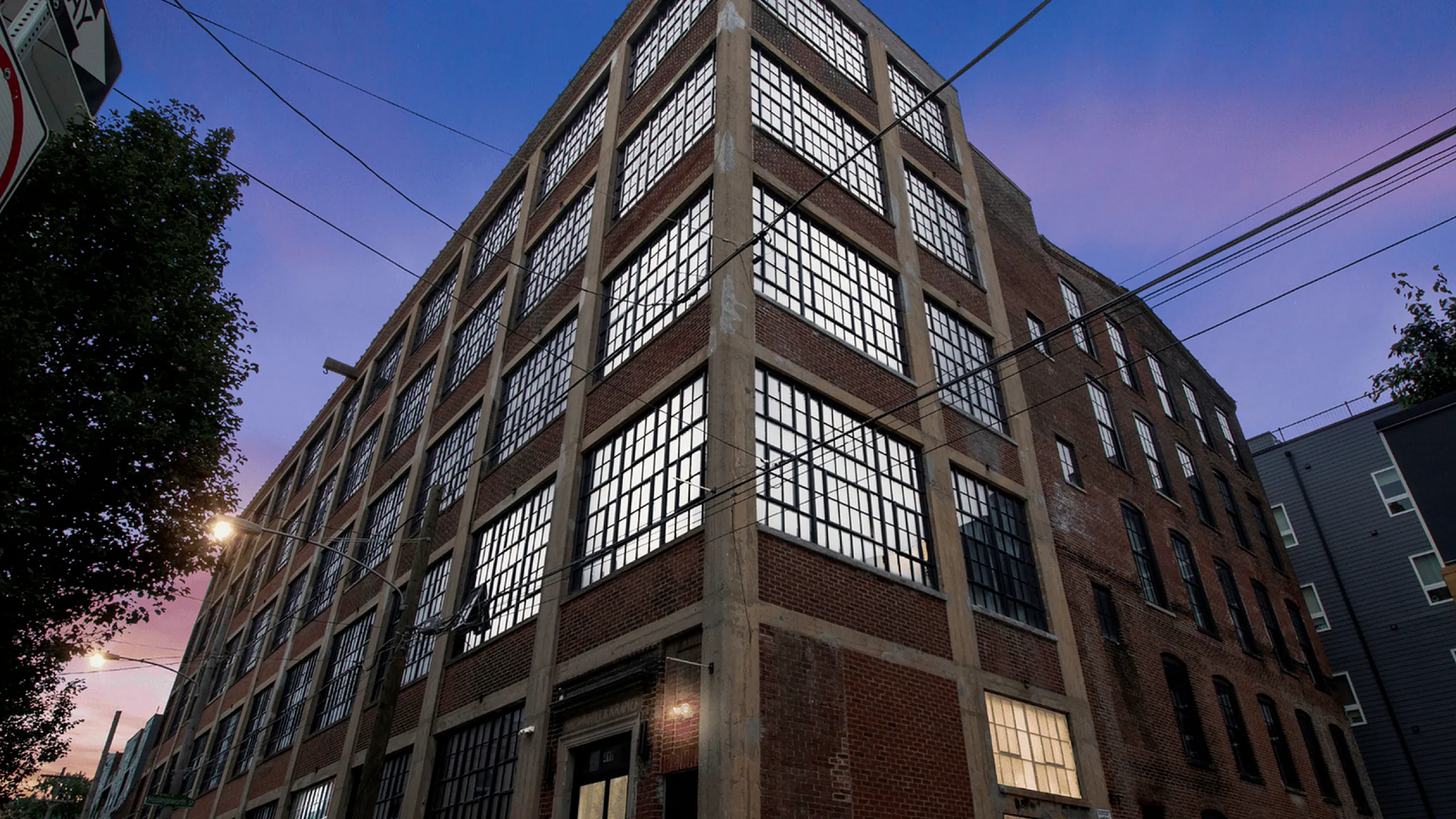 Stylish brick loft building with large industrial windows at dusk.