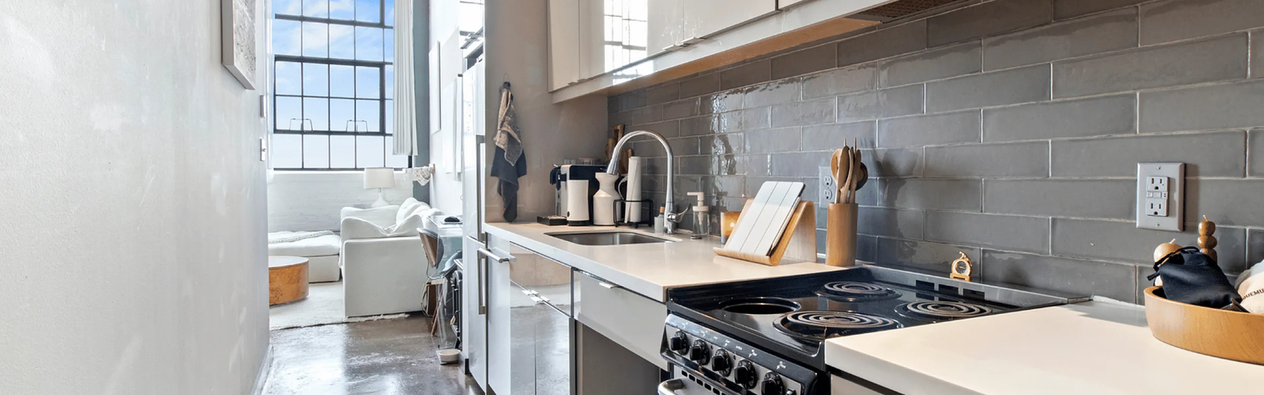 Sleek kitchen with stainless steel appliances, modern cabinets, and a view into a bright living area with large windows.