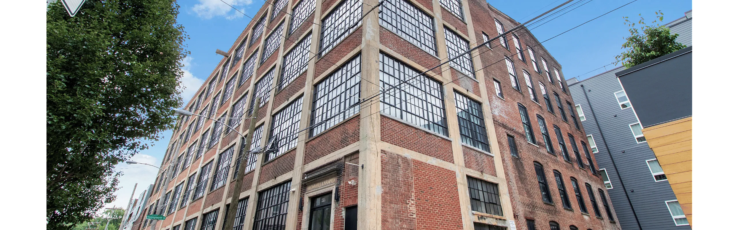 Industrial-style brick building with large grid windows and a corner view under a clear blue sky.