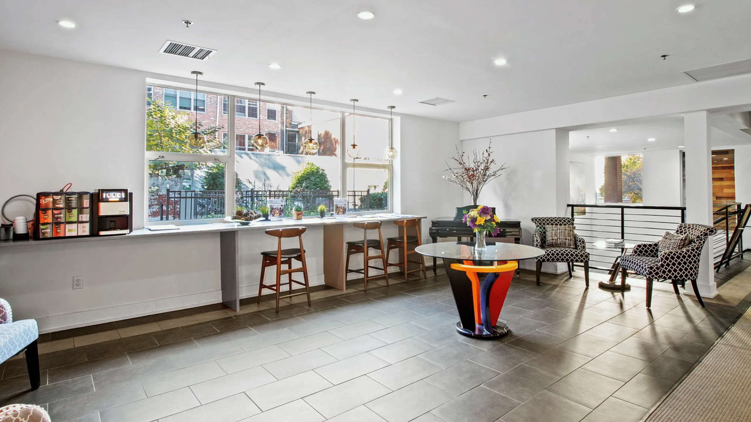Spacious, sunlit lounge with modern seating, colorful decor, and a coffee station.
