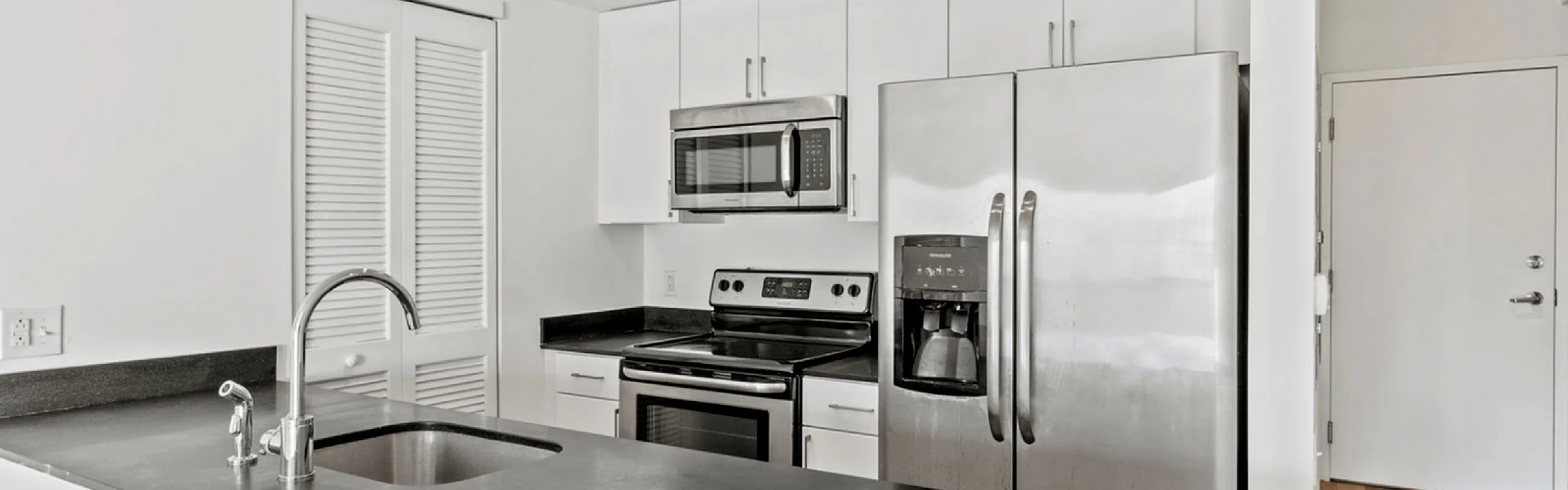 Modern kitchen with stainless steel appliances and black countertops.