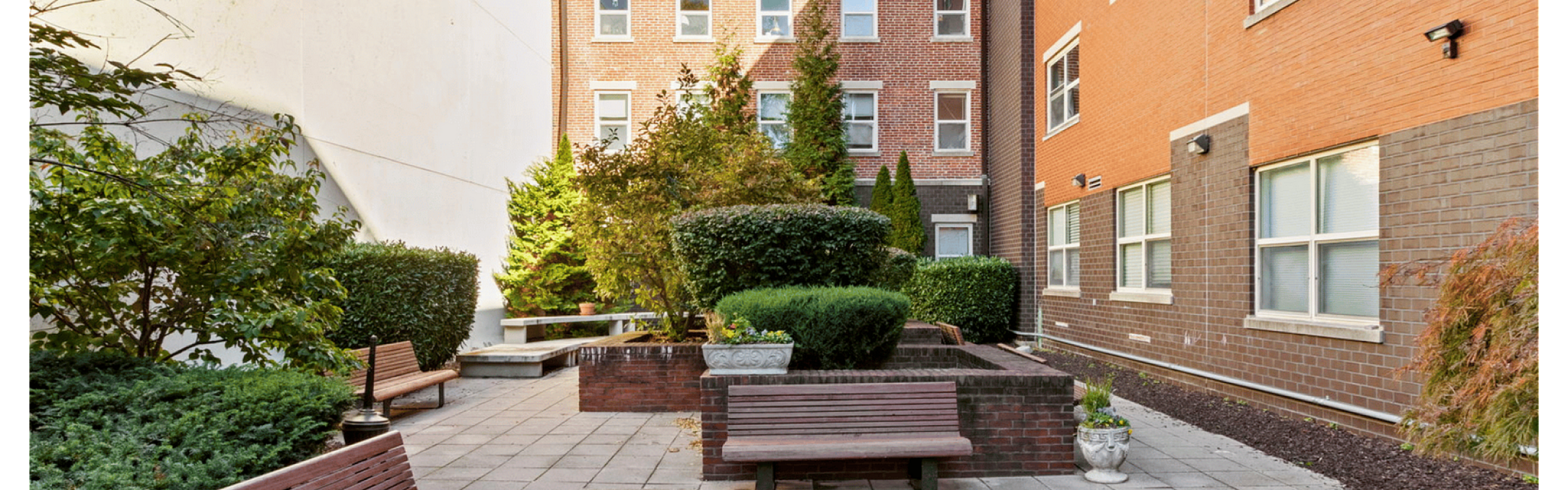 Charming courtyard with benches, greenery, and a brick building backdrop.