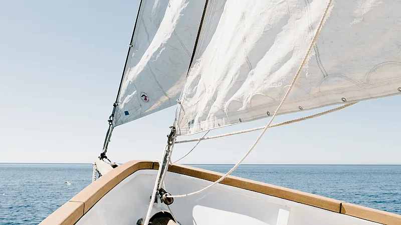 Close-up view of a boat's deck and sails against a clear blue sea and sky.