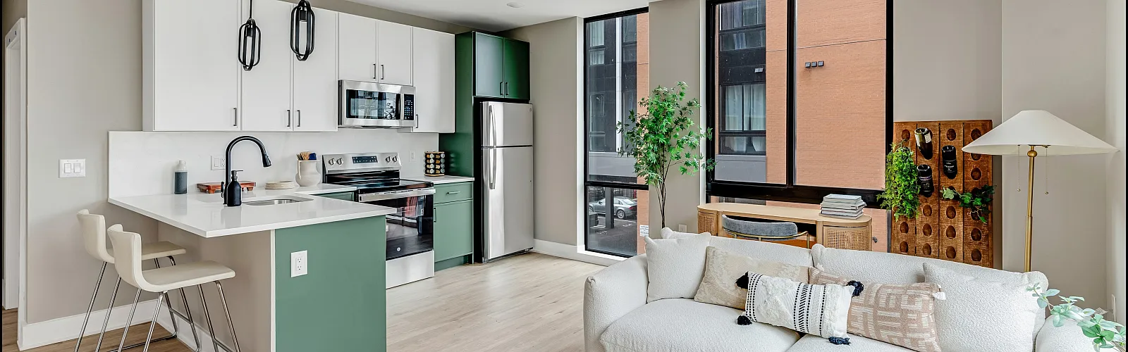 Modern, open-concept living area with stylish kitchen, sleek appliances, and elegant decor. Natural light floods the cozy seating area featuring a plush white sofa and contemporary accents.