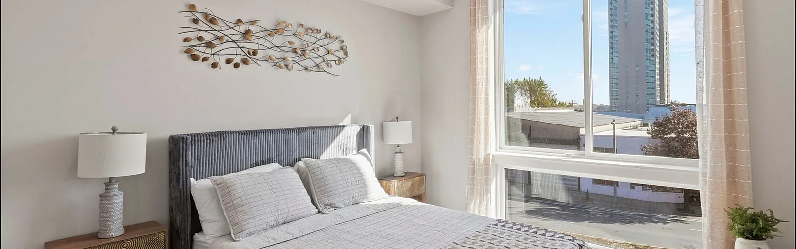Bright and inviting bedroom with modern decor, large windows offering city views, and stylish furnishings.