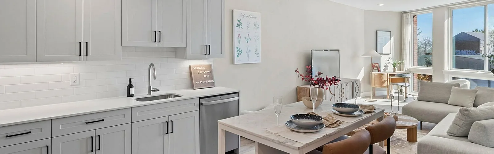 Contemporary open-plan living area with sleek grey kitchen, stylish dining space, and cozy lounge, illuminated by large windows.