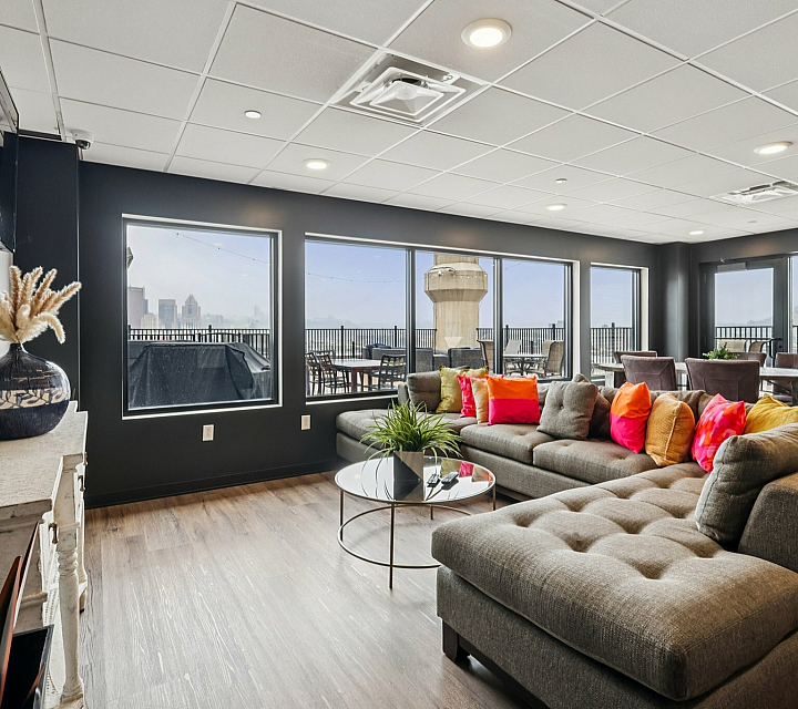 Chic apartment lounge with vibrant pillows on a plush sectional sofa, expansive windows showcasing a stunning cityscape view, and elegant contemporary decor.