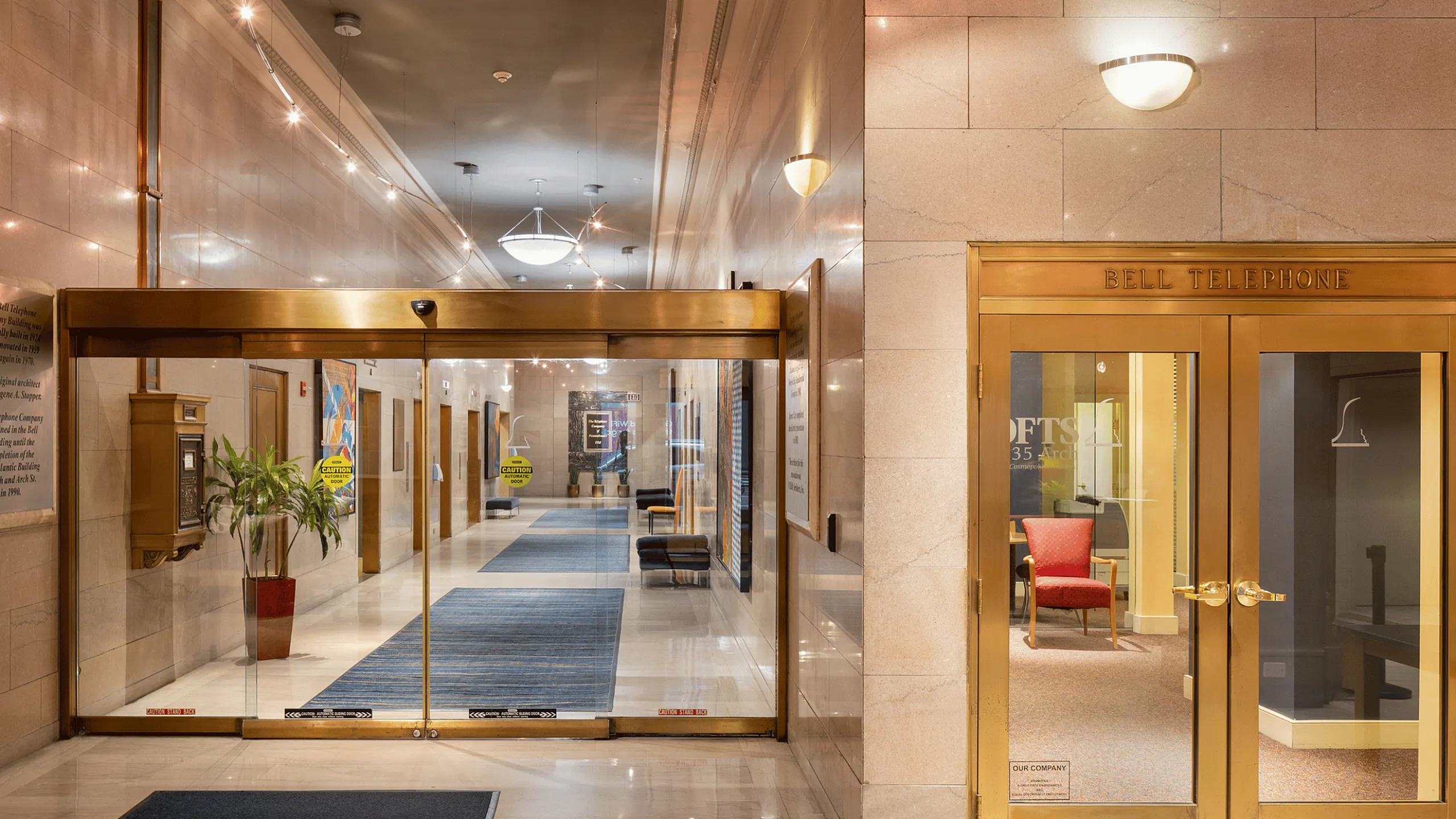 Elegant building lobby with gleaming glass entry and stylish lighting, featuring luxurious marble walls and a welcoming seating area.