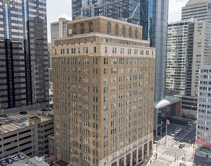 Elegant historic brick building surrounded by modern skyscrapers in an urban cityscape.