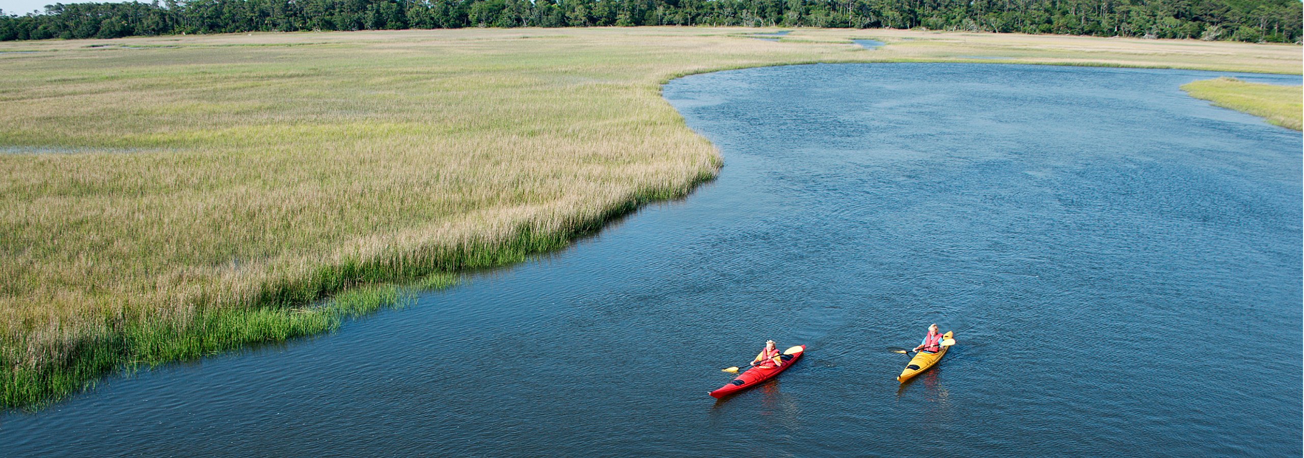 Serene waterway with two colorful kayaks in a lush, grassy landscape.