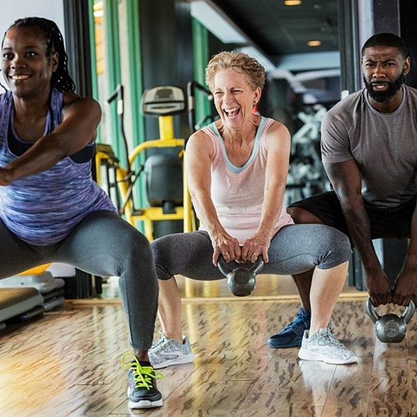 Three individuals performing squats with kettlebells in a gym setting, showcasing strength and fitness training.