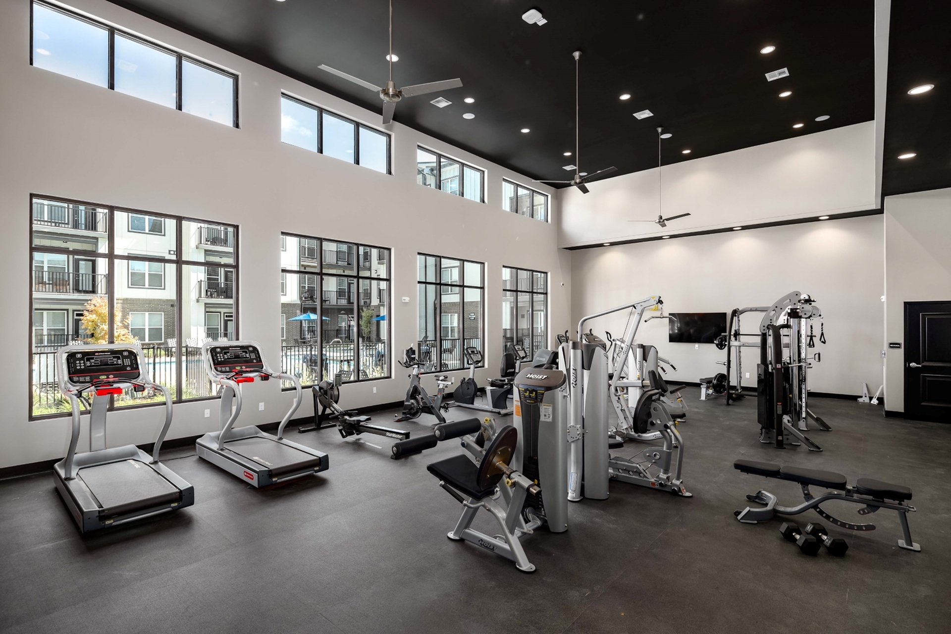 A gym featuring cardio equipment and weights, located in a building with large windows that allow natural light to flood the space at at Abberly Alston Apartment Homes and Townhomes in Cary, NC