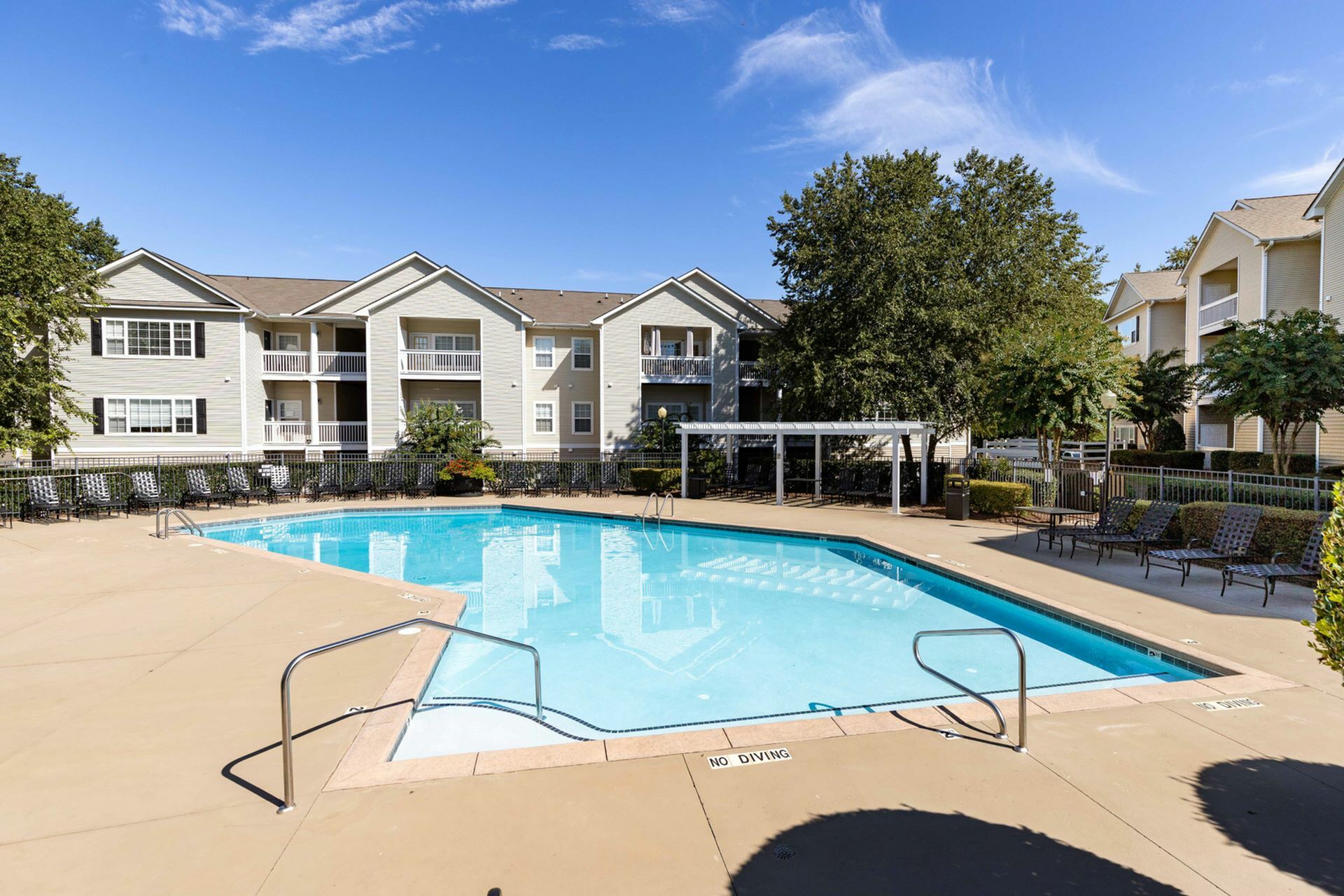 Outdoor swimming pool with a spacious sundeck, surrounded by lounge chairs, a pergola-shaded seating area, and landscaped greenery, with apartment buildings in the background at Abberly Woods Apartments in Charlotte, NC