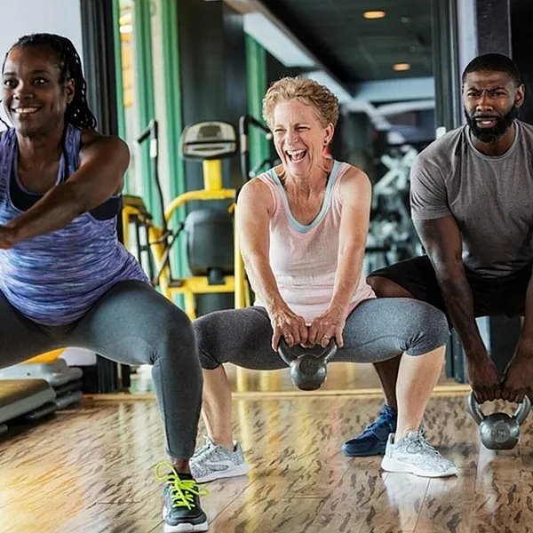 Energetic group fitness class with diverse individuals lifting kettlebells on polished wooden flooring, emphasizing community and wellness.