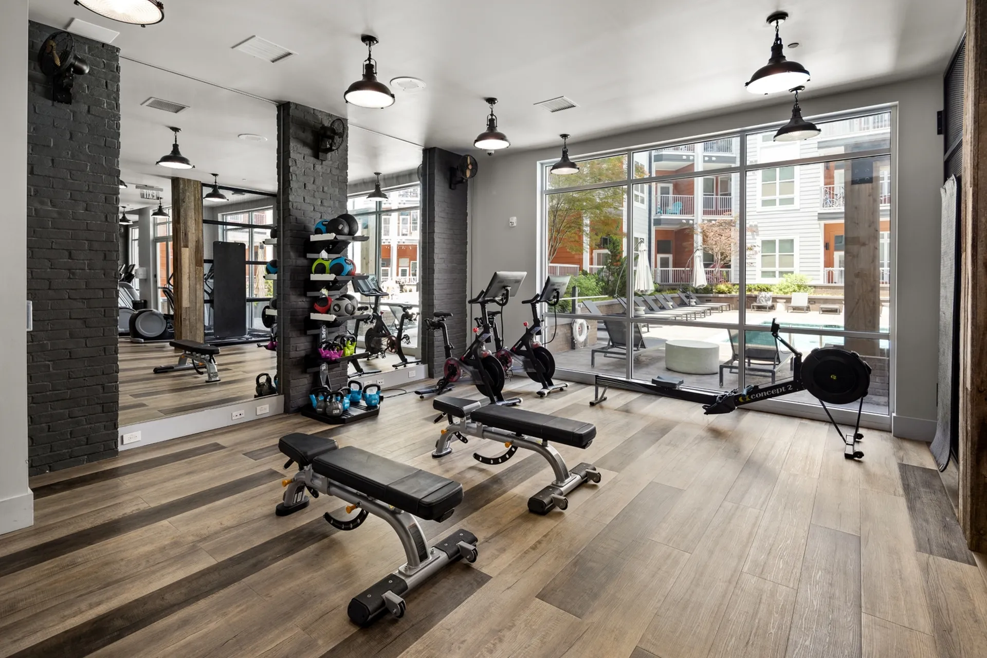 Modern apartment gym with large windows showcasing exercise equipment and a view of the outdoor pool area.