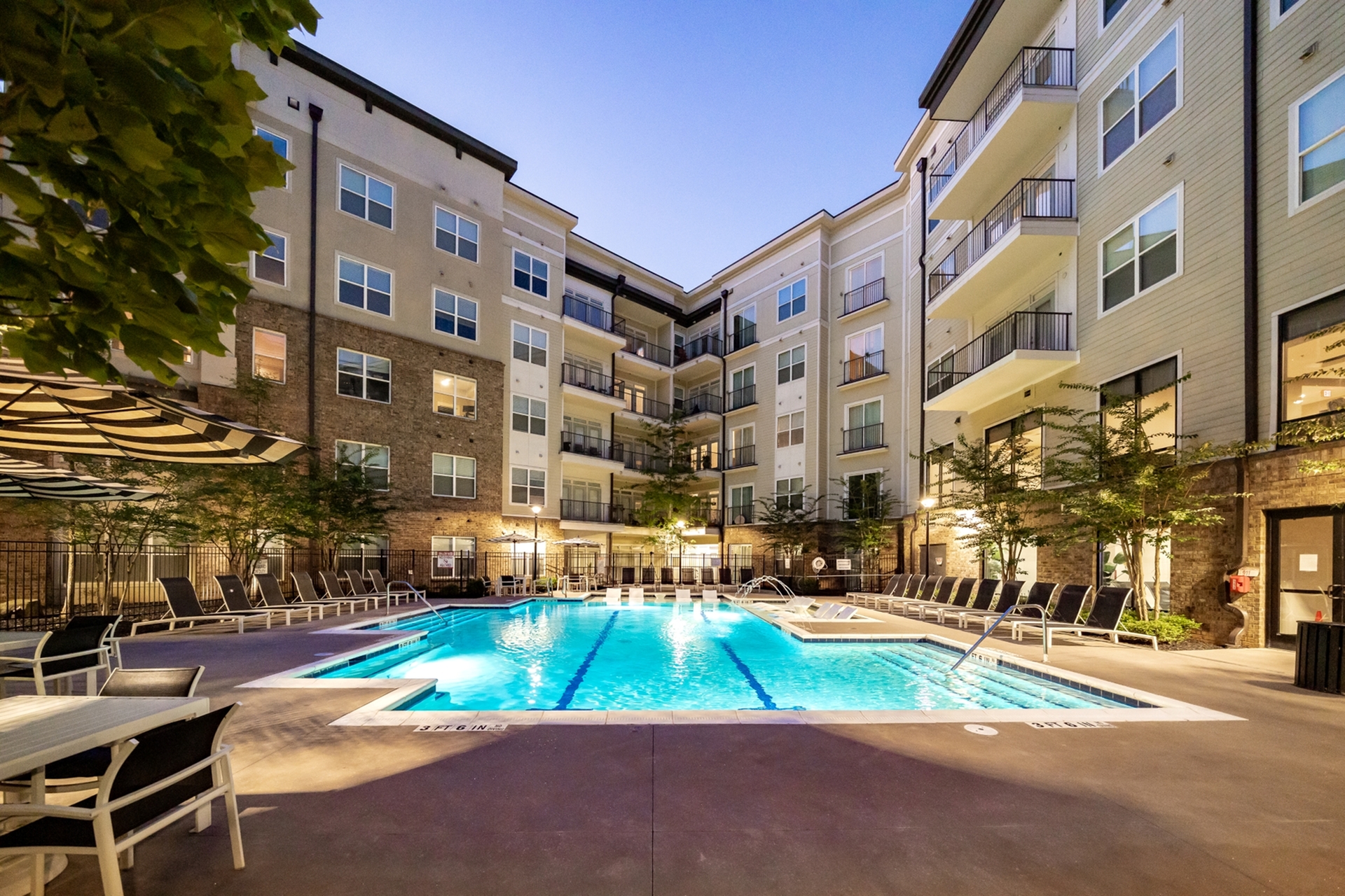 Elegant apartment complex featuring a sparkling outdoor pool surrounded by stylish lounge chairs and modern architecture.