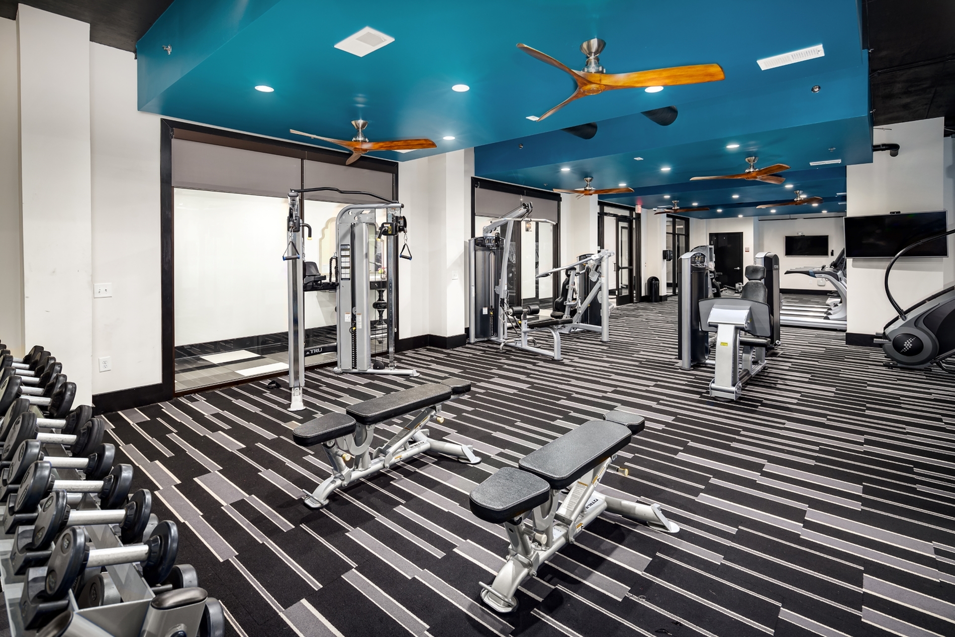 Modern fitness center with sleek equipment, vibrant ceiling fans, and a contemporary striped carpet enhancing the workout experience.