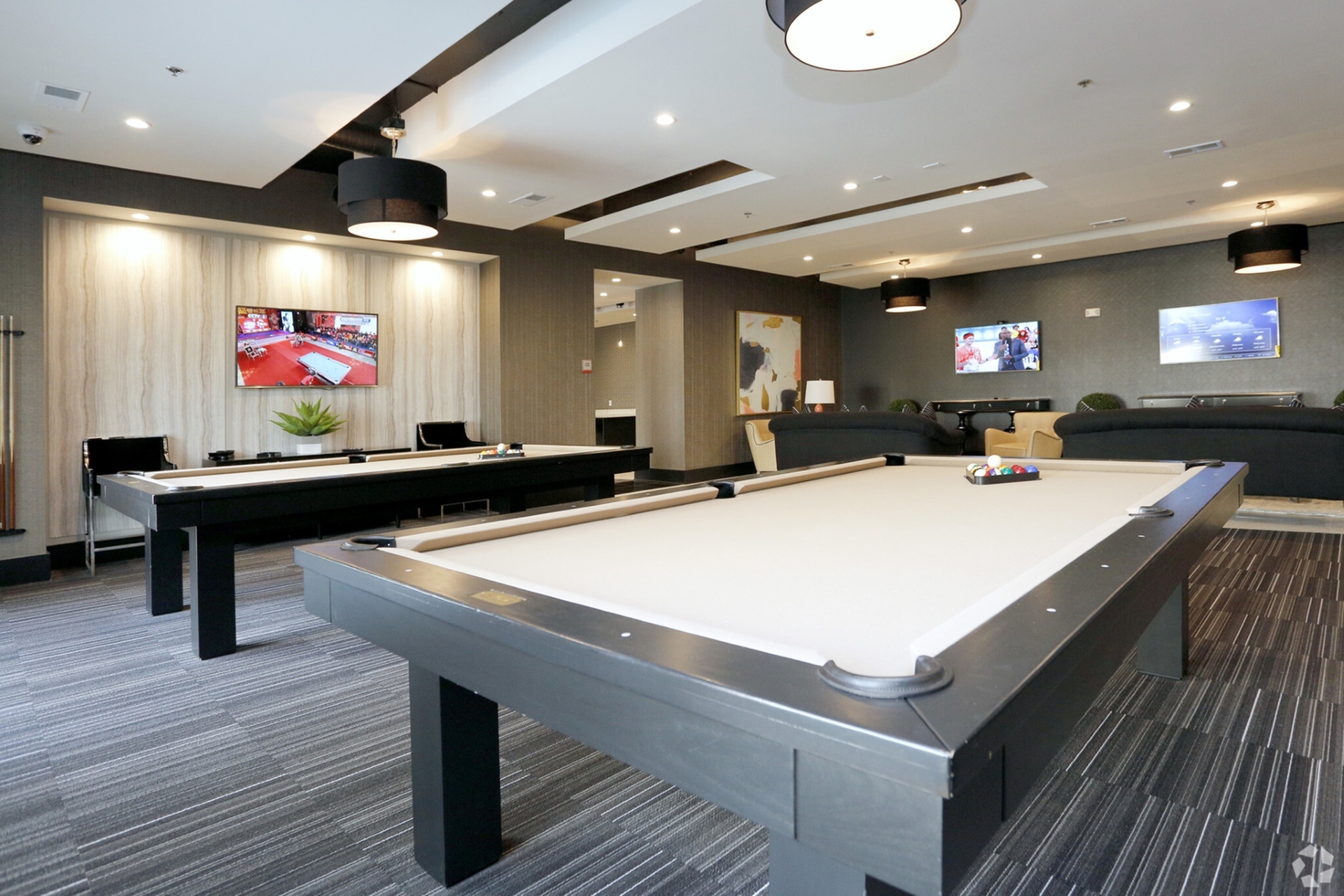 Luxurious game room featuring modern pool tables, stylish lounge seating, and large flat-screen TVs, offering a perfect entertainment space.