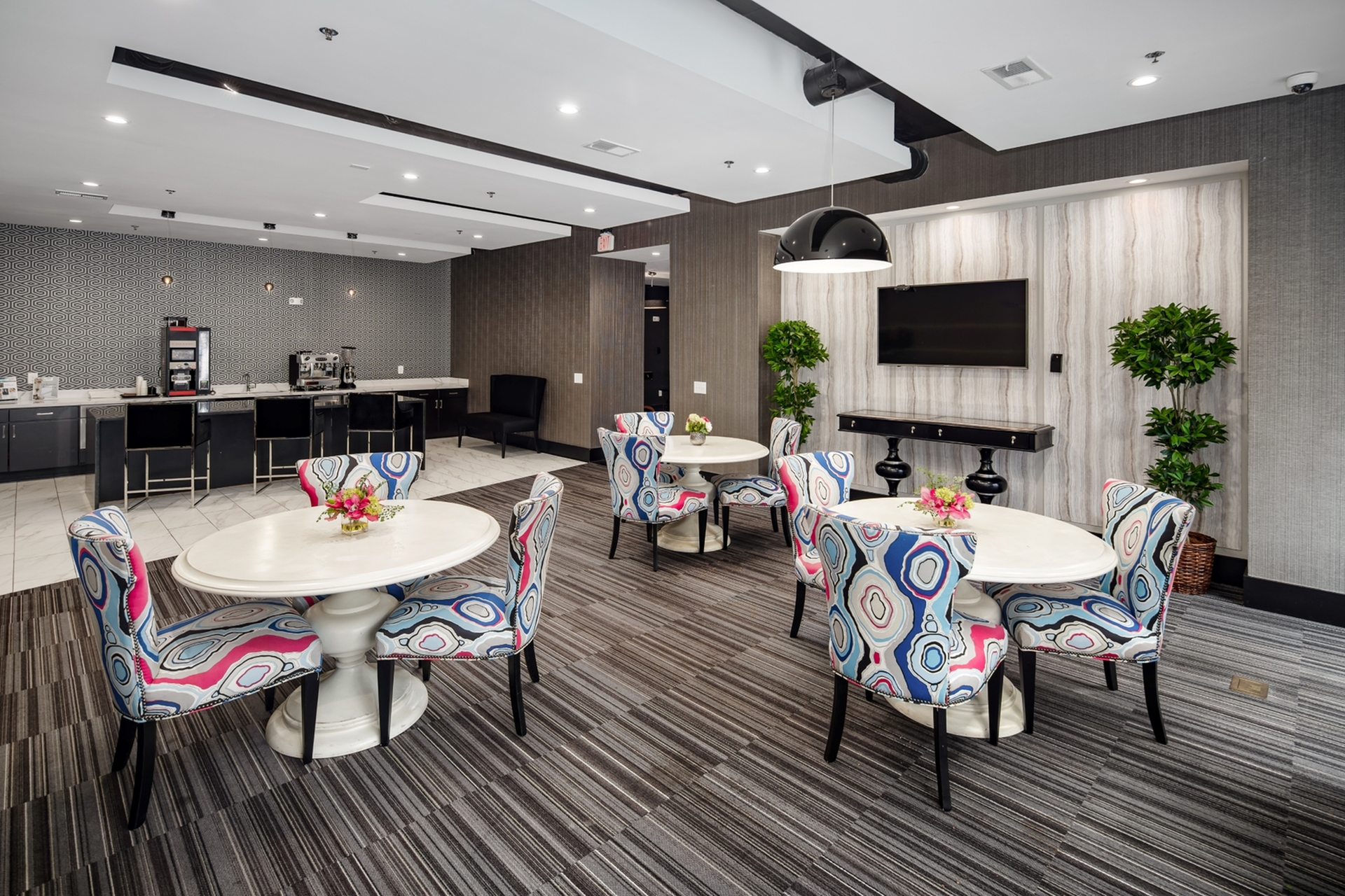 Elegantly designed communal space featuring vibrant patterned chairs, sleek modern decor, and a well-equipped coffee station.