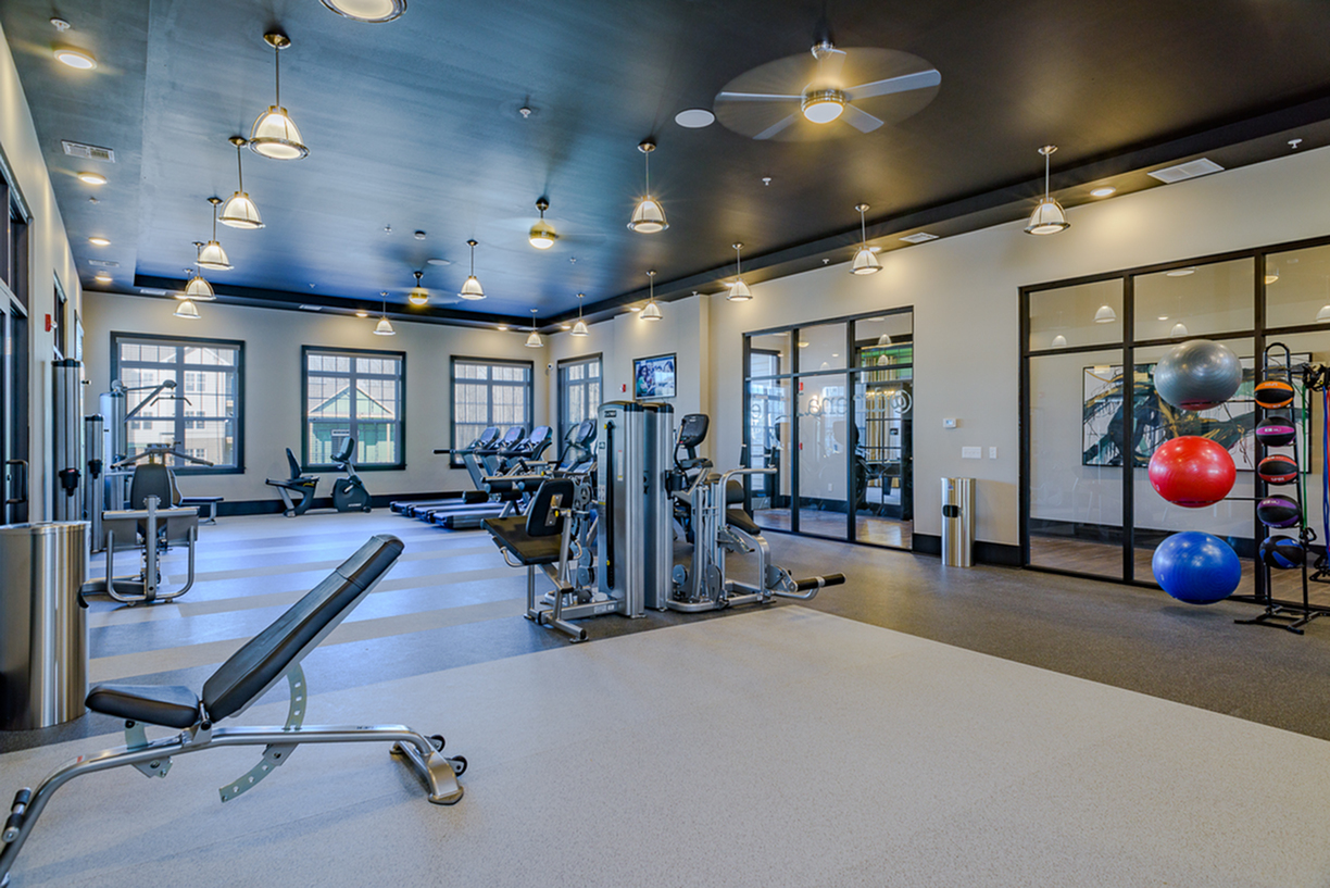 Modern fitness center with state-of-the-art exercise equipment, bright lighting, and a sleek black ceiling design for an invigorating workout experience.