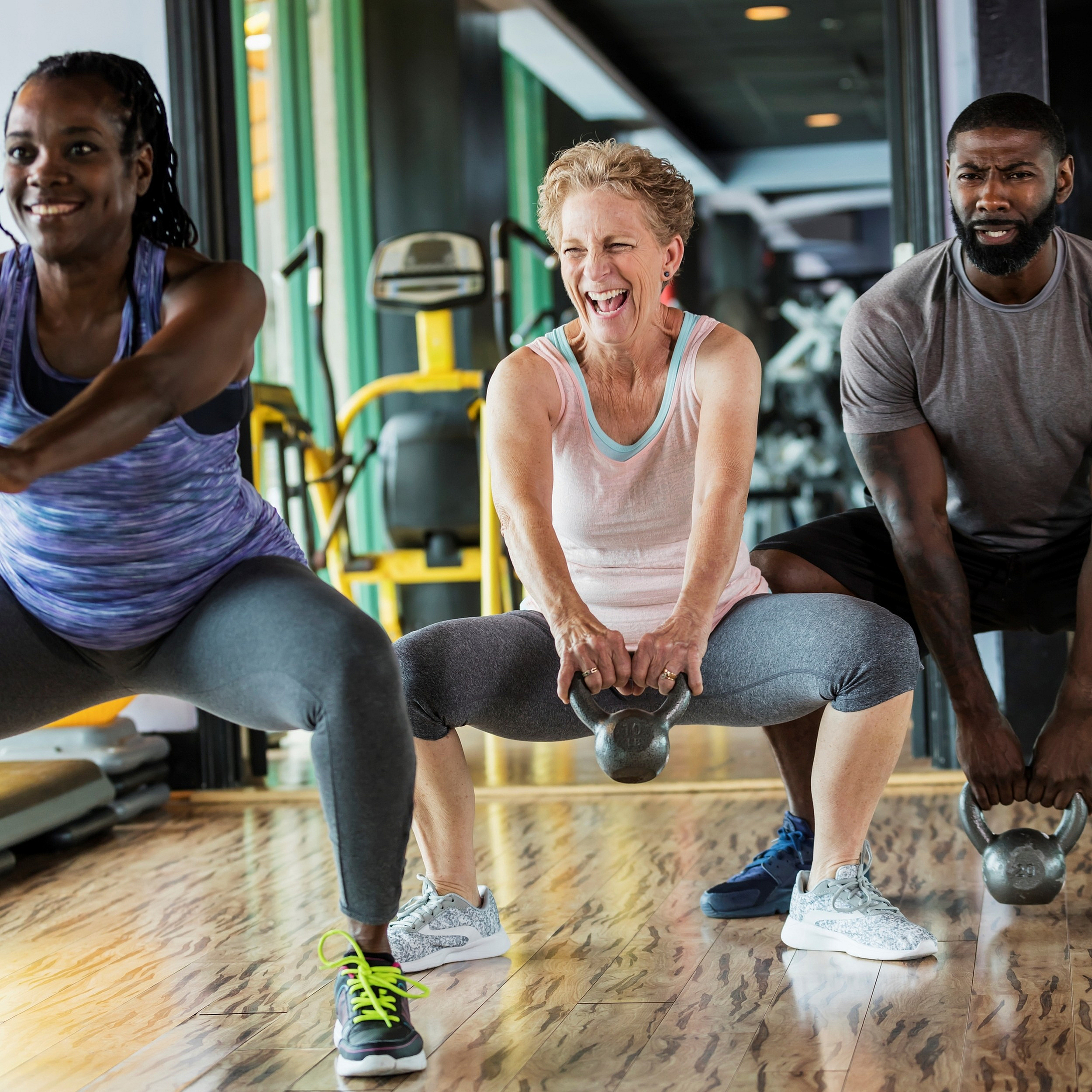 Energetic group workout session with diverse individuals lifting kettlebells on sleek wood flooring, reflecting a motivating and inclusive gym environment.