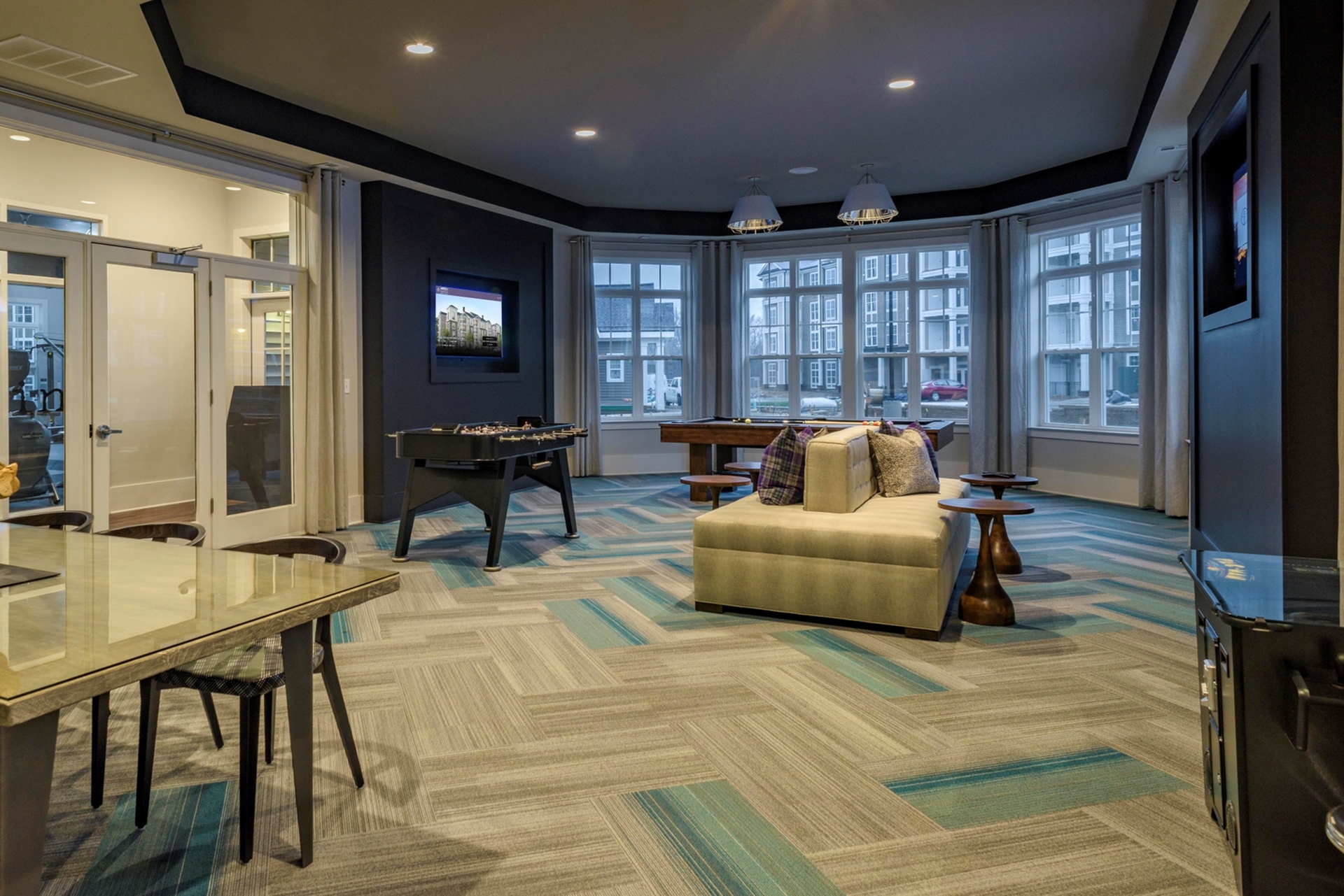 Elegant open-concept lounge with modern decor, featuring cozy seating, a foosball table, and large windows offering natural light.