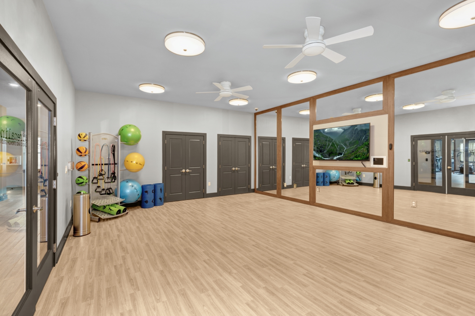 Spacious exercise studio with sleek wood flooring, mirrored wall, and vibrant fitness equipment, designed for an energizing workout experience.