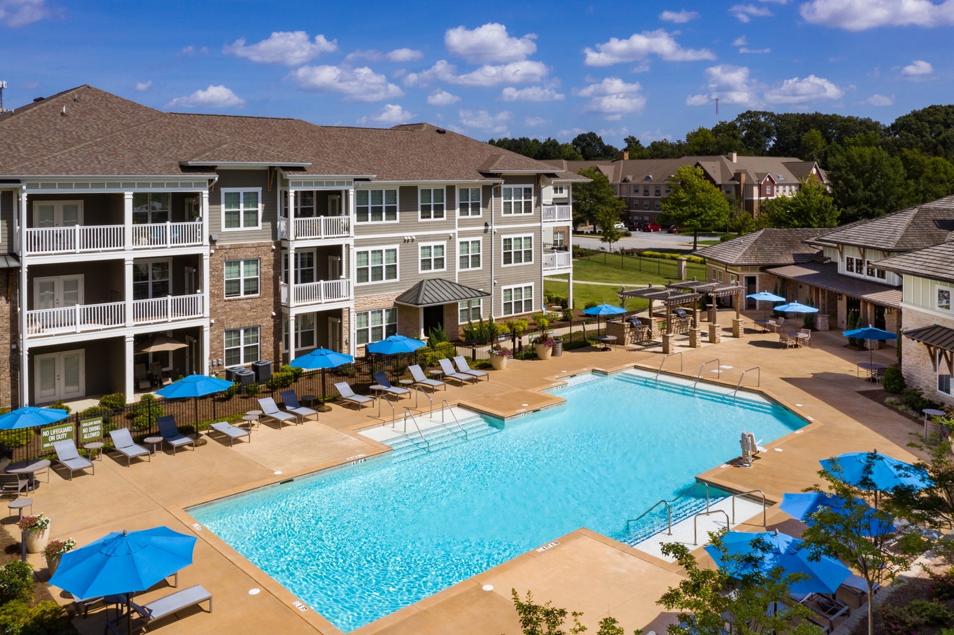 Charming apartment complex with resort-style pool, sun loungers, and spacious balconies under a bright blue sky.
