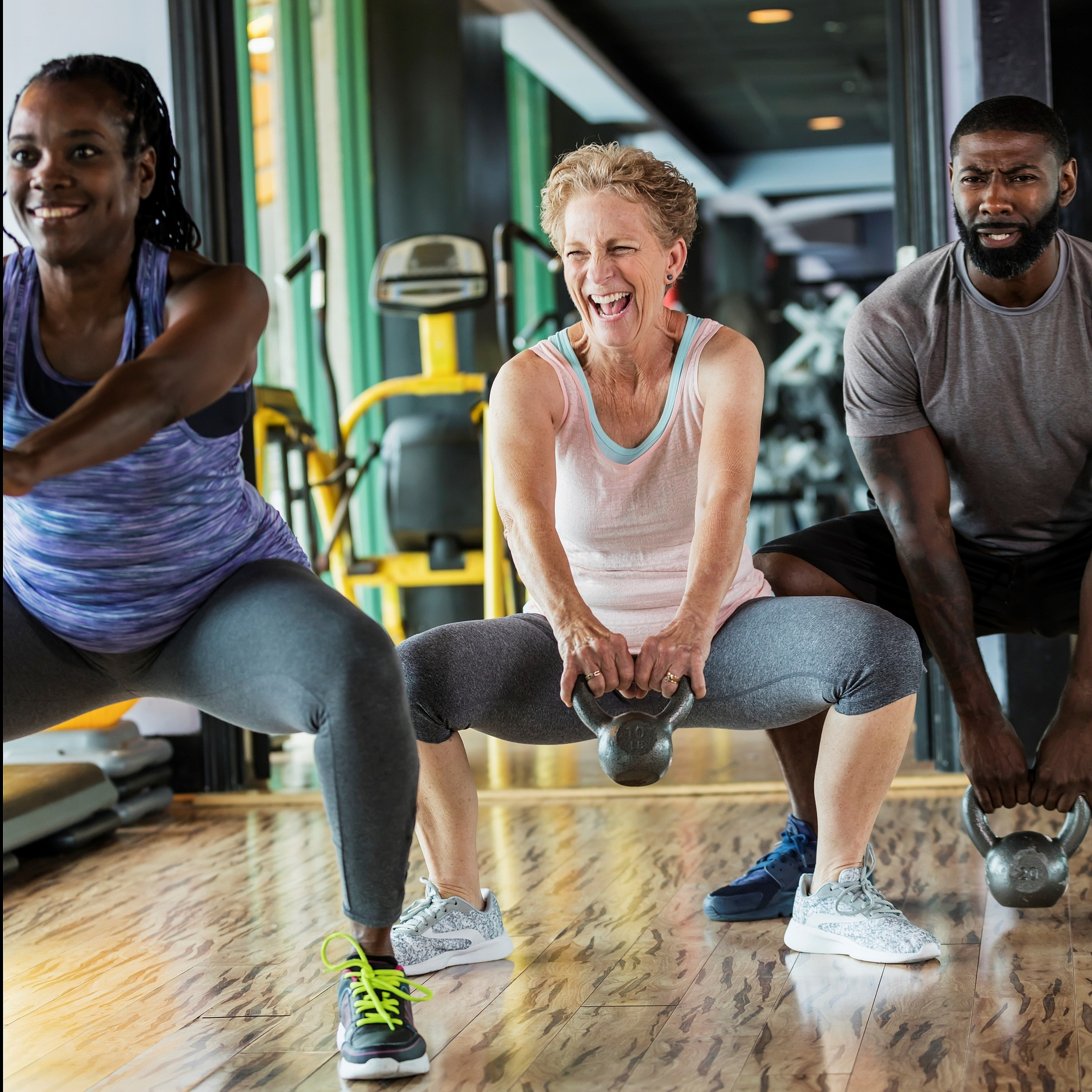 Energetic group exercise session with diverse participants using kettlebells in a modern, well-lit gym.