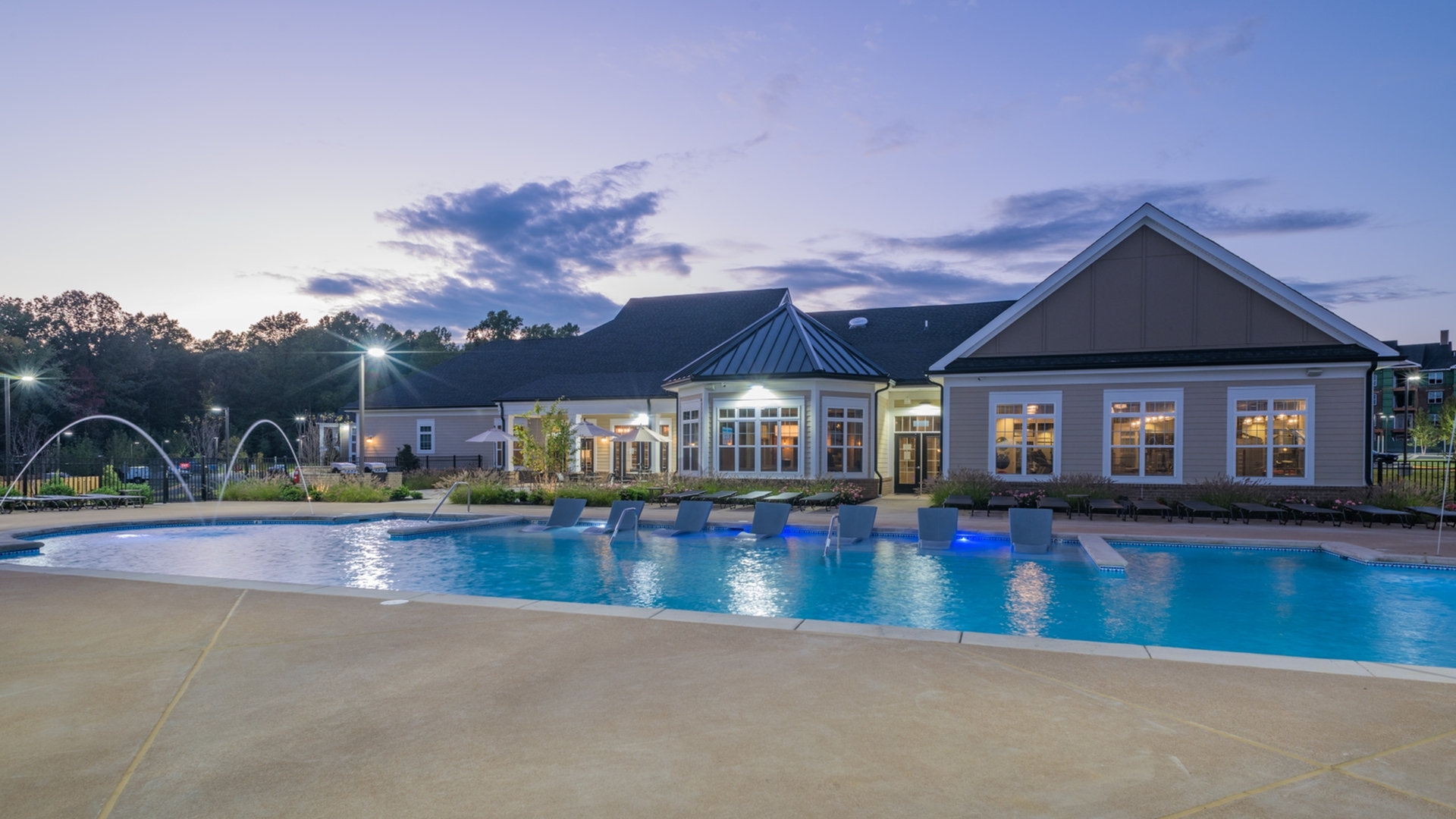 Elegant dusk view of a luxurious apartment complex with a sparkling outdoor pool and inviting lounge chairs.